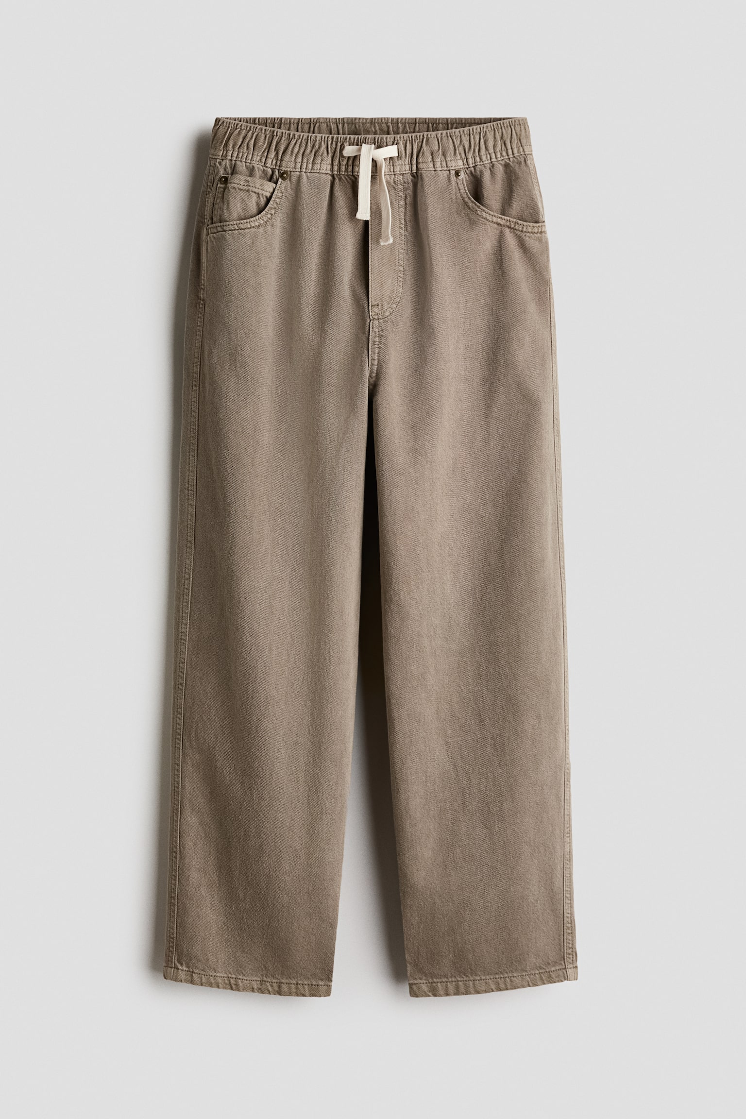Ces joggers en sergÃ© de coton taupe sont prÃ©sentÃ©s de face, mettant en valeur une silhouette ample Ã  jambe droite. Ils prÃ©sentent une taille Ã©lastiquÃ©e froncÃ©e avec un cordon de serrage blanc cassÃ©, une fausse braguette surpiquÃ©e et un style classique Ã  cinq poches.