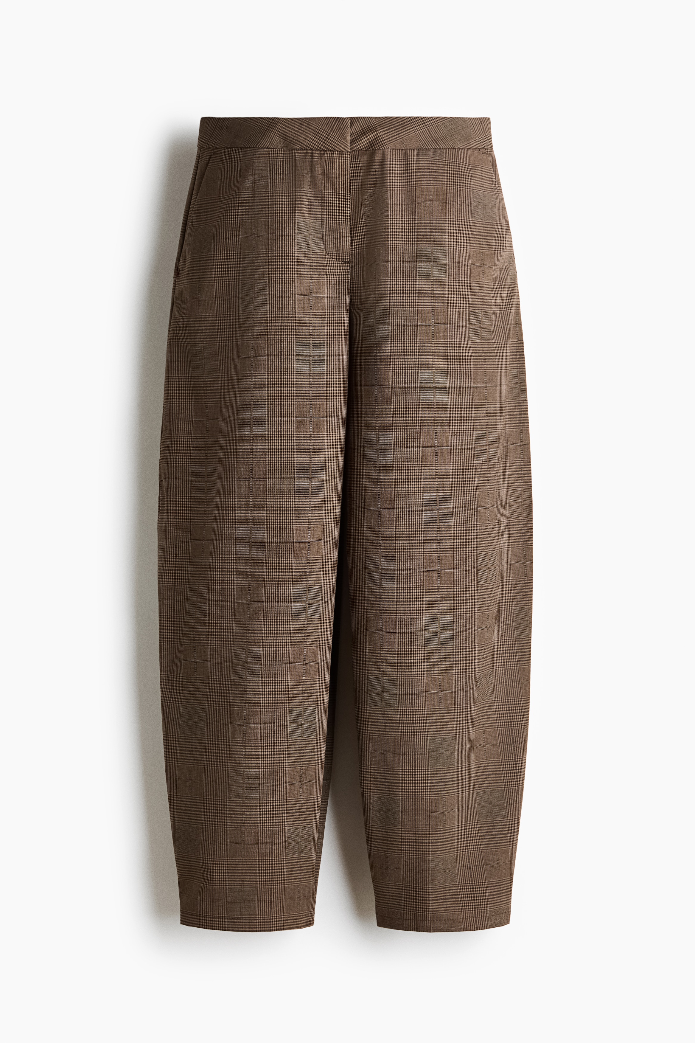 Braon pantalone sa dezenom, krojene u opuÅ¡tenom kroju sa barrel nogavicama i dijagonalnim boÄnim dÅ¾epom, nosi model. Pantalone su stilizovane uz crni gornji deo dugih rukava, belu potkoÅ¡ulju, crne patike i tamnu tote torbu koju model nosi u ruci.