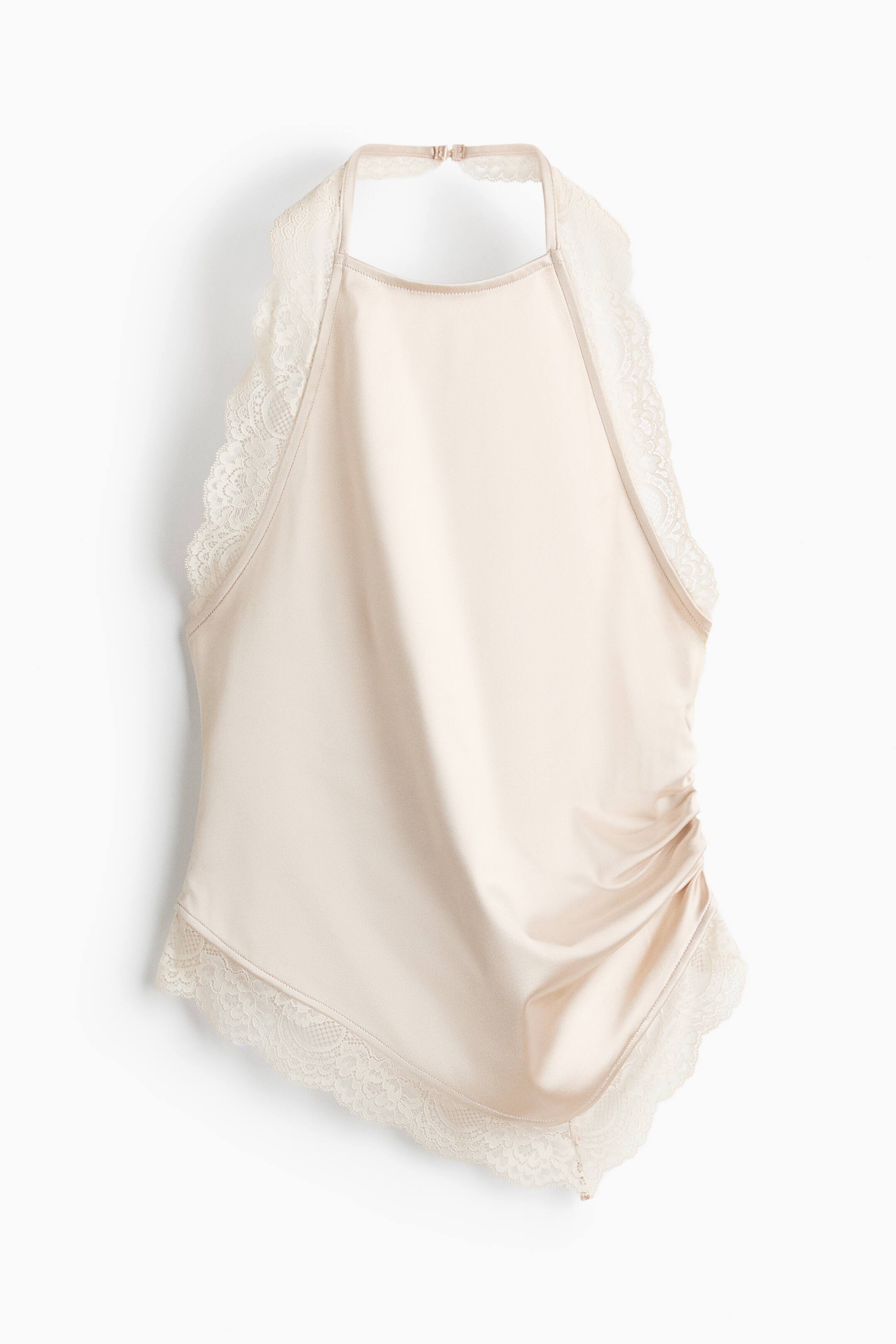 View larger image: A light beige satin halter-neck top is shown front-facing, featuring delicate scalloped lace trim along the neck strap and the asymmetrical hem. The top has gathered ruching on one side, creating a draped effect across the front.