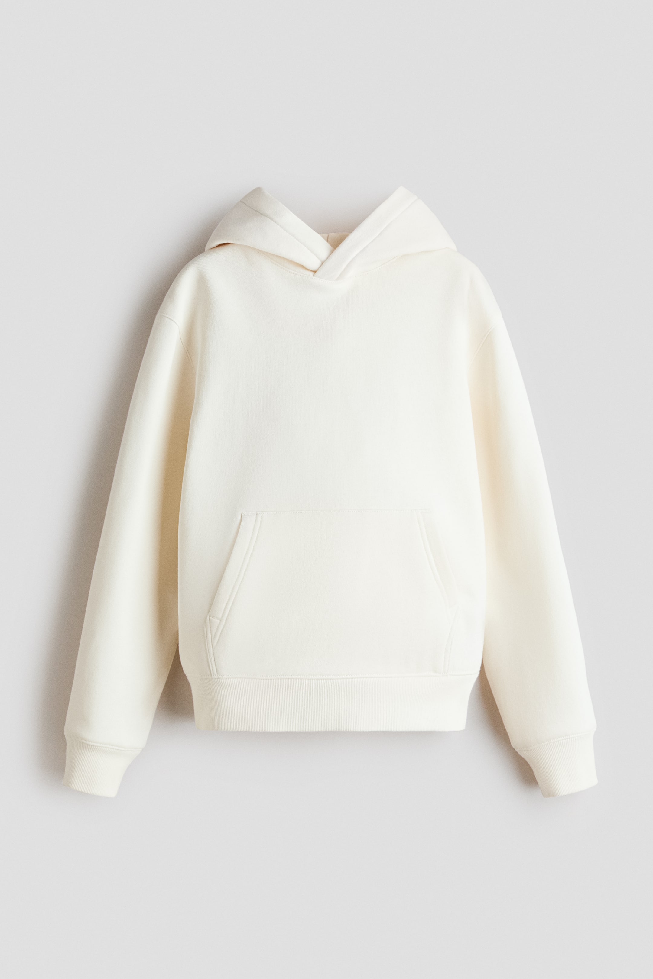 Ver imagen más grande: La sudadera con capucha de color crema está de frente, mostrando una capucha forrada de jersey con un detalle cruzado, hombros ligeramente caídos, mangas largas, un bolsillo canguro, puños acanalados y un dobladillo acanalado.