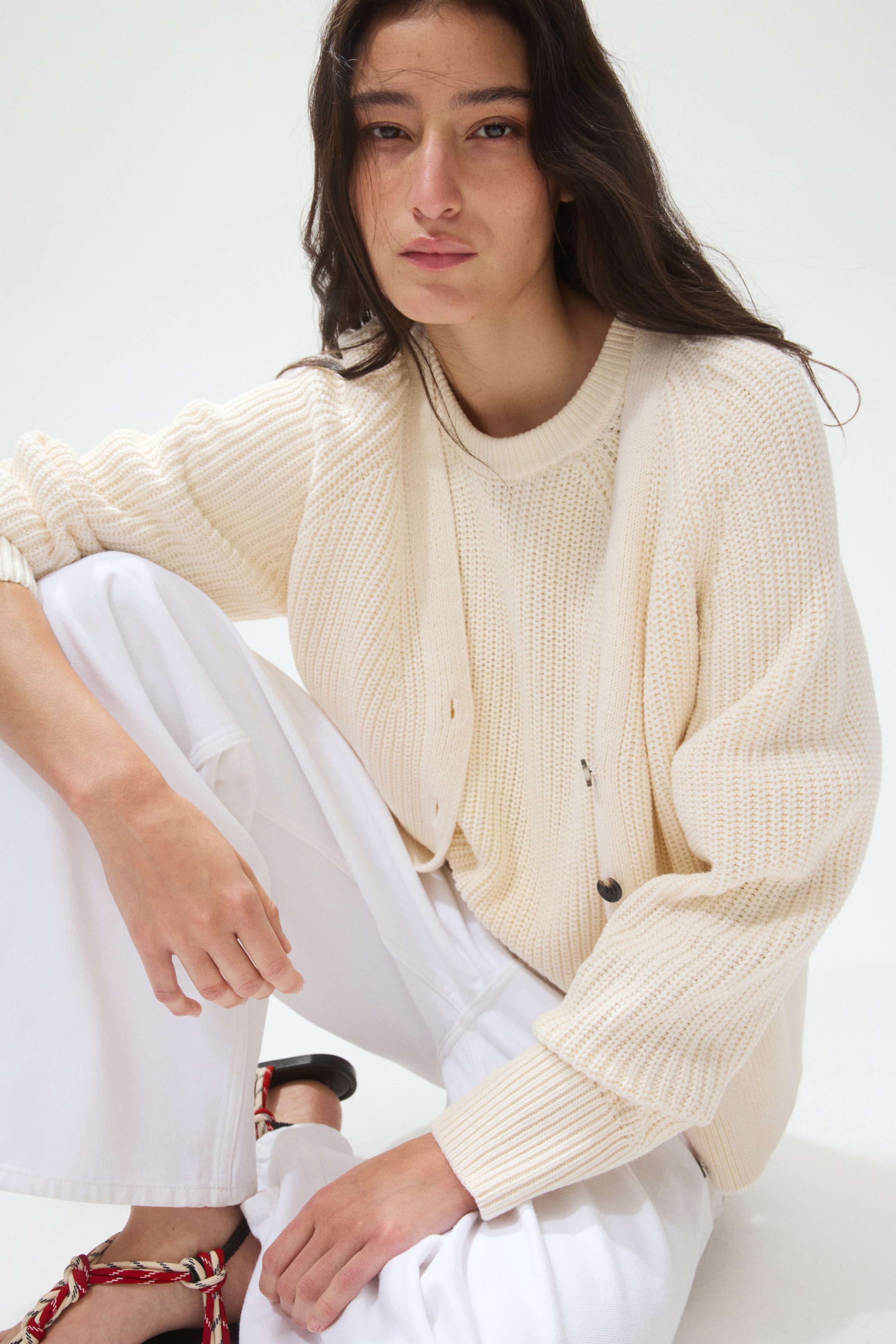 View larger image: A cream-coloured ribbed knit cardigan is worn open over a matching ribbed knit crewneck jumper. The cardigan features long sleeves with ribbed cuffs and visible front buttons.