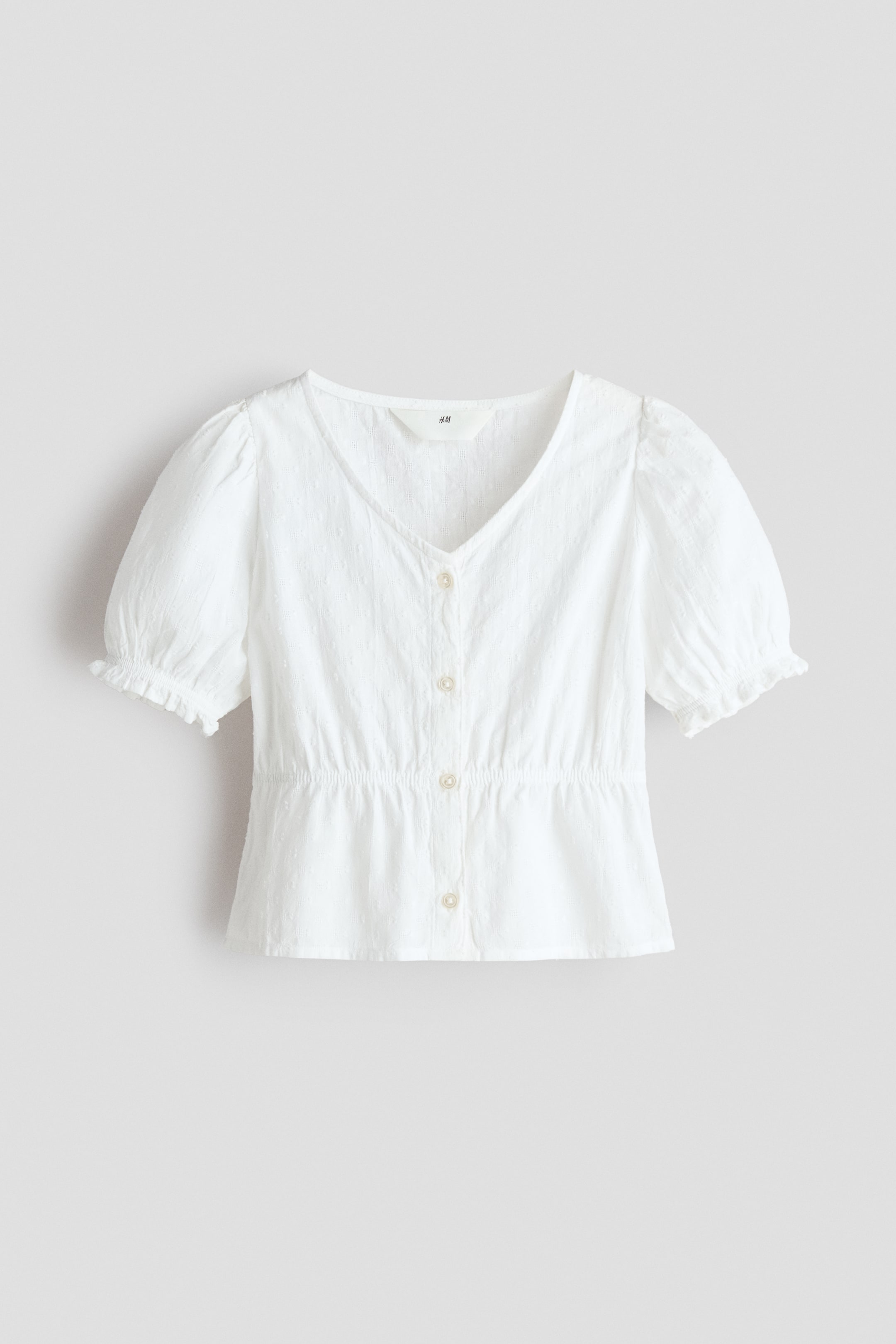 View larger image: A white airy cotton seersucker blouse showcases its front, highlighting a V-shaped neckline and buttons running down the center. It is crafted with short puff sleeves featuring elasticated, frill-trimmed cuffs and a narrow elasticated waistline.