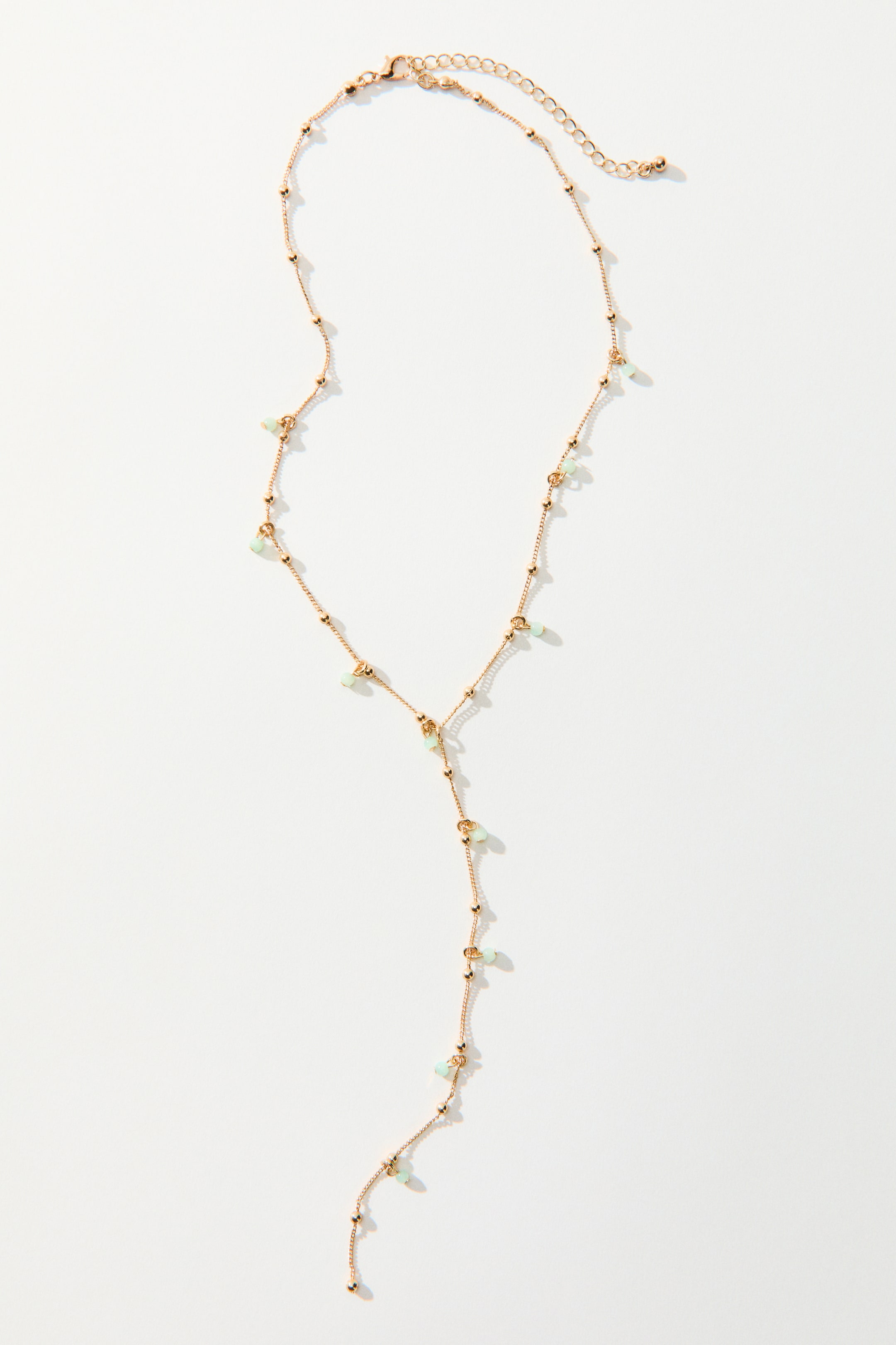 Agrandir l'image: Le collier est une chaîne délicate de ton doré, ornée de petites perles sphériques et de perles vert clair de forme irrégulière espacées le long de sa longueur. Il forme un style Y-lariat, avec un fermoir mousqueton et une chaîne d'extension visible en haut.