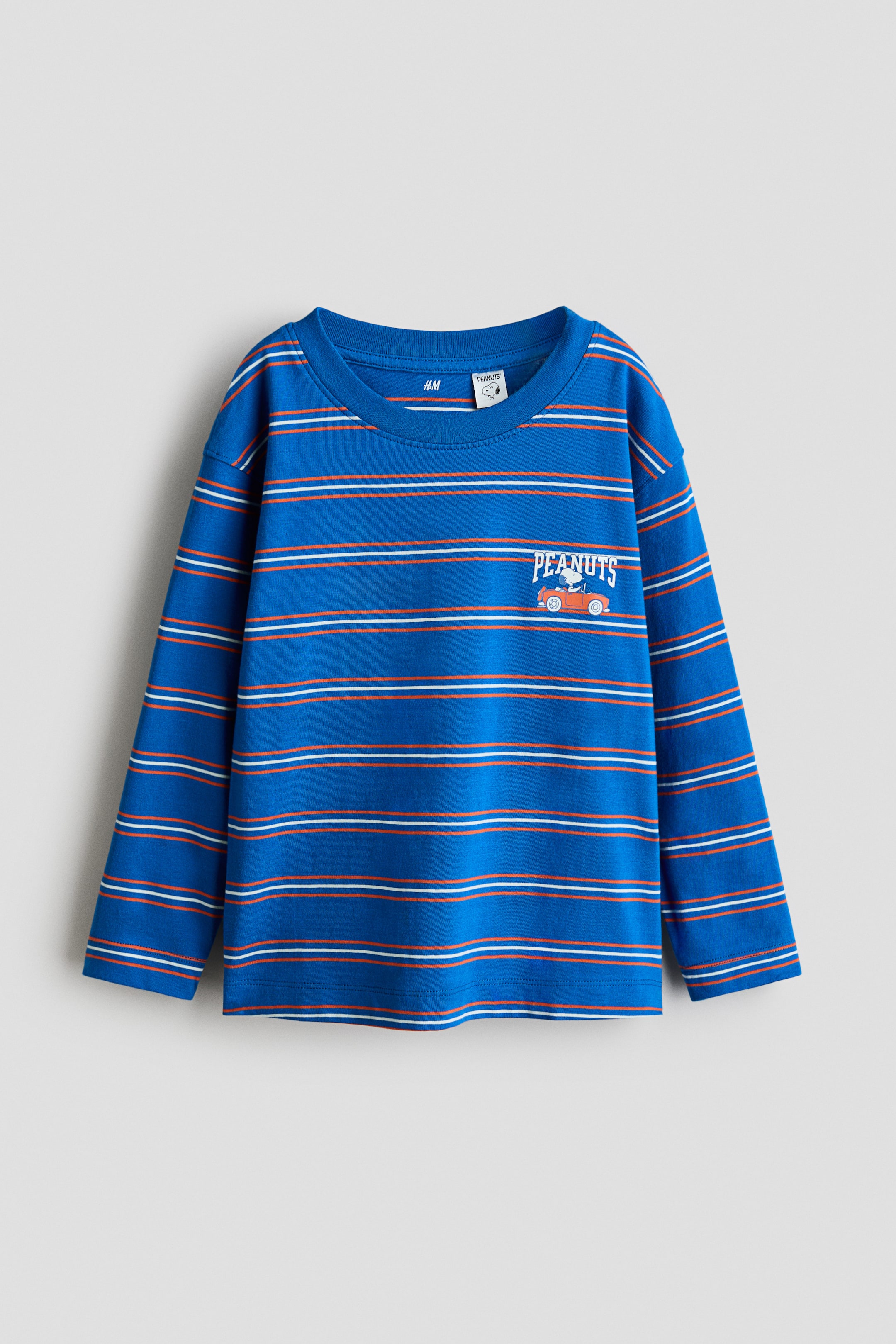 拡大画像を表示: 正面に配置された長袖の丸首Tシャツ。青を基調に、オレンジと白の細い横ストライプが入っています。前面には「PEANUTS」の刺繍と、その下で小さなオレンジ色の車を運転するスヌーピーのデザインが施されています。