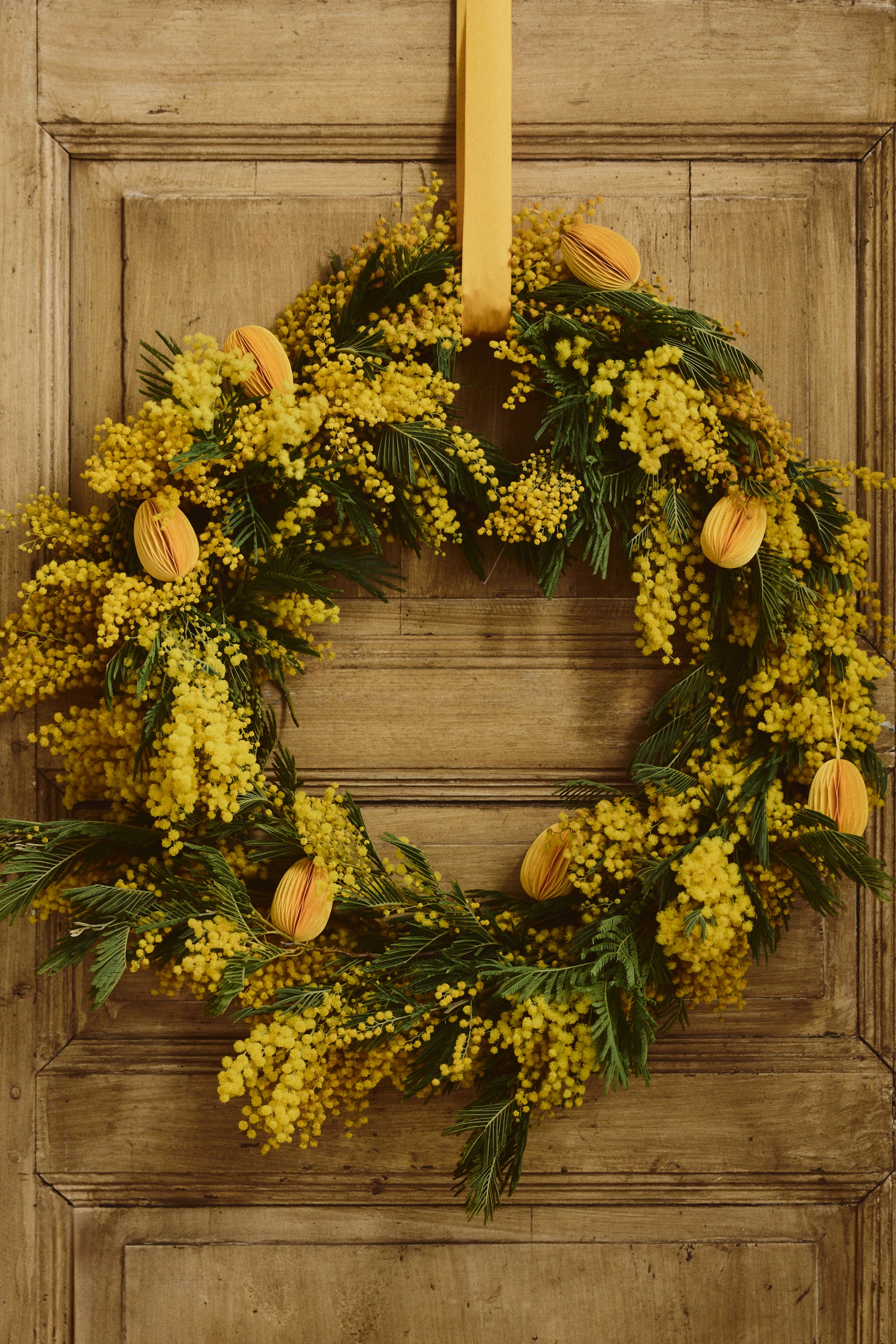 Grotere afbeelding bekijken: Eivormige, kartonnen decoraties hebben een geribbelde, waaiervormige constructie in een oranje-gele tint. Een stoffen koord hangt elke decoratie op aan de bovenkant, met elk een hoogte van ongeveer 7 cm.