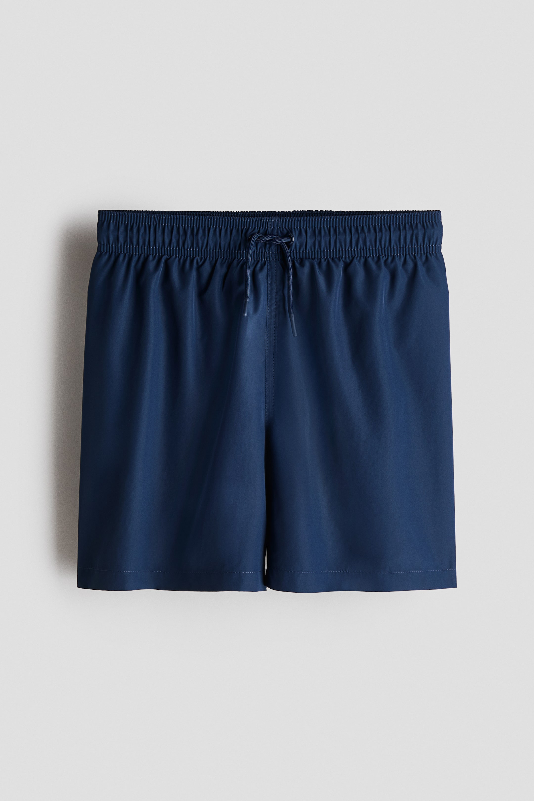 View larger image: Dark blue swim shorts are facing front, featuring an elastic waistband with a drawstring closure tied at the center.