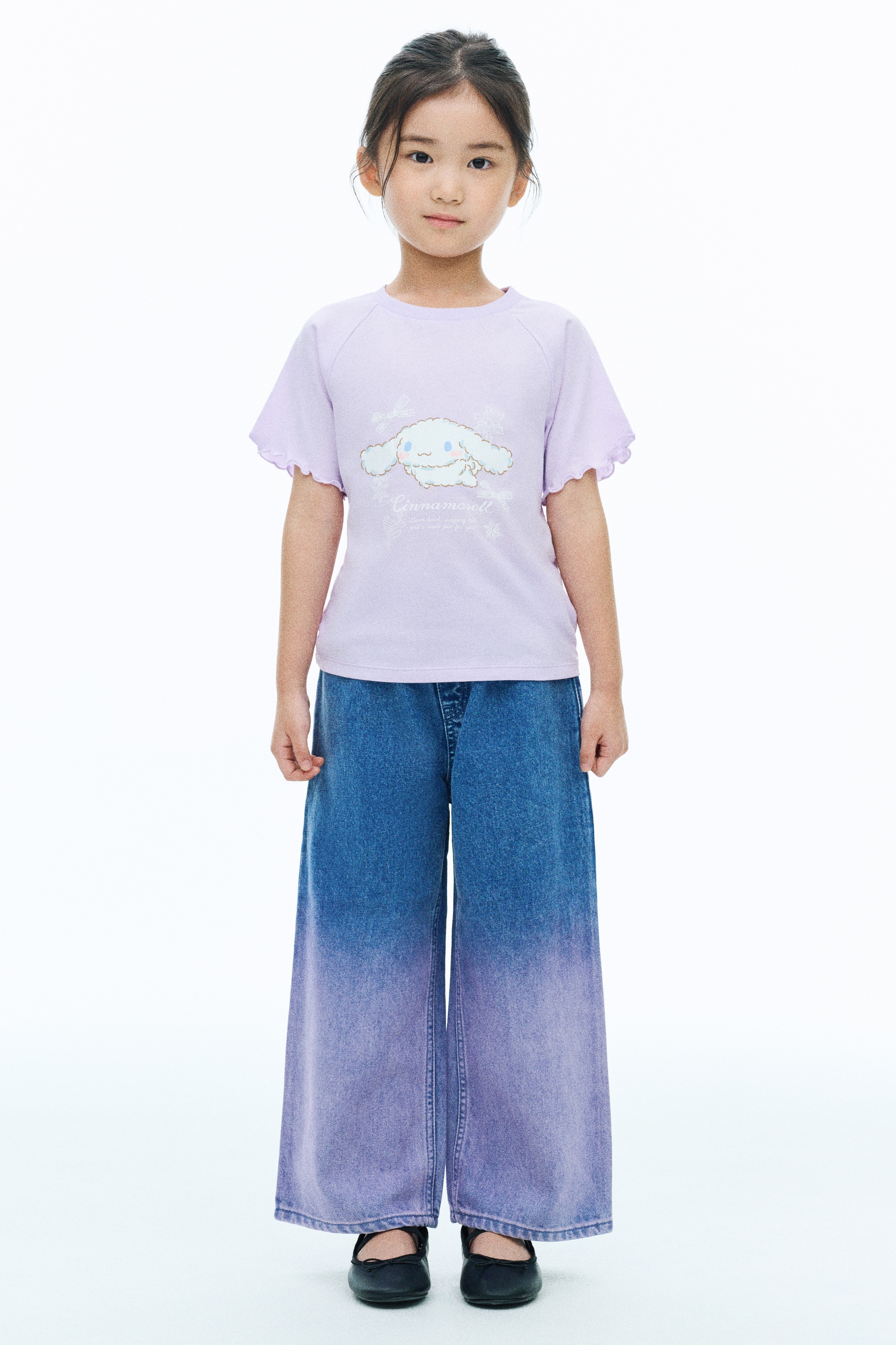 A light purple short-sleeve sweatshirt is shown from the front, featuring a ribbed crew neck and raglan sleeves with wavy lettuce-edge hems. The centre displays a graphic print of the character Cinnamoroll surrounded by white bows and snowflakes, with the name "Cinnamoroll" printed in cursive below.
