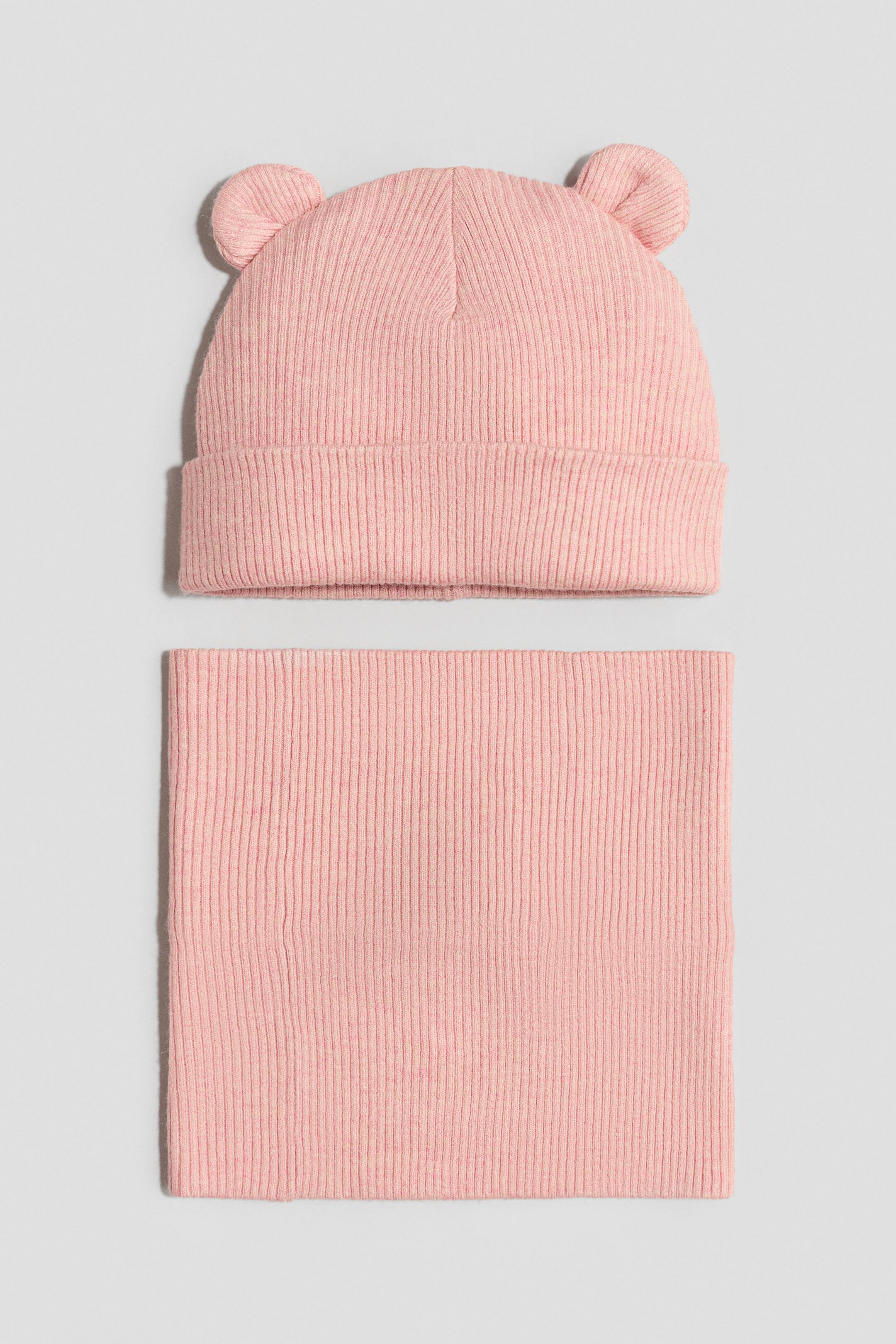 View larger image: A light pink ribbed knit hat and a matching neck warmer are laid flat, oriented vertically. The hat features a folded brim and two small, rounded ear-like protrusions on top, while the rectangular neck warmer is placed below it.
