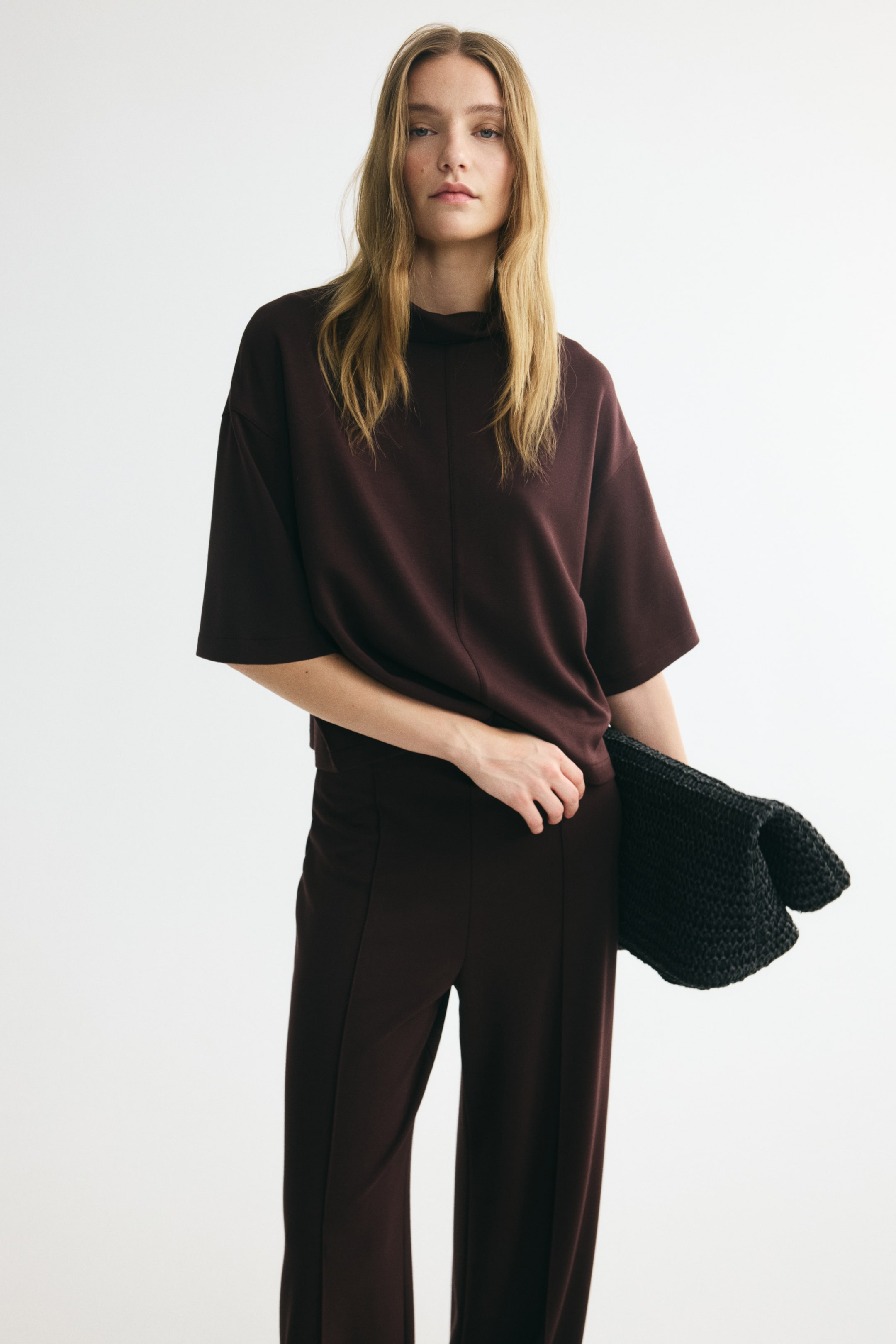 View larger image: A matching set of a top and trousers in heavy stretch jersey is shown from the front. The top features a turtleneck, a visible seam running down the front, dropped shoulders, and 3/4-length sleeves, while the trousers have straight legs with sewn-in creases down the front.