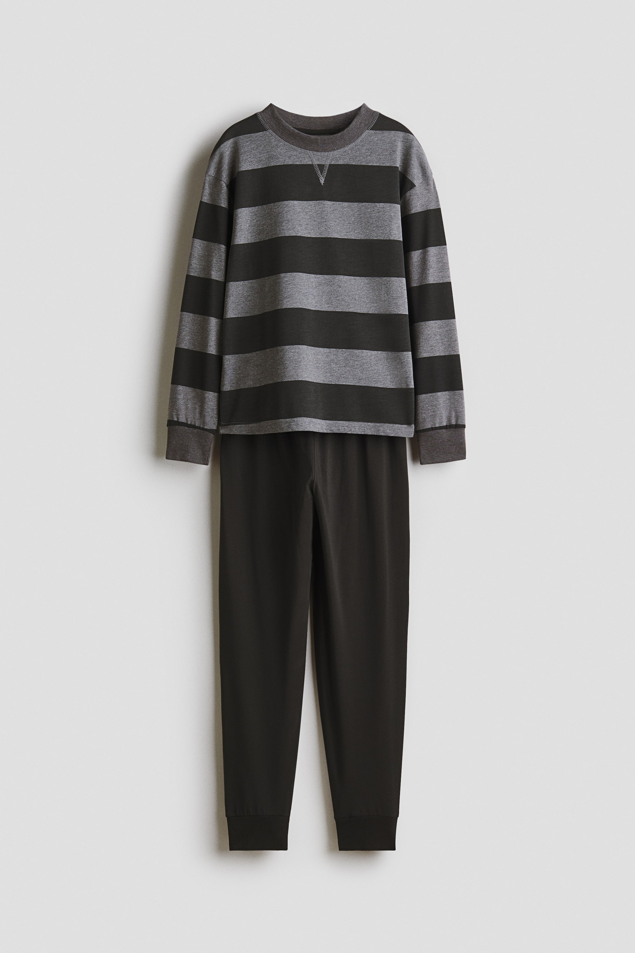 Ver imagen más grande: Un conjunto de ropa de descanso de dos piezas se presenta de frente. La parte superior de manga larga presenta rayas horizontales alternas en gris oscuro y gris claro, con un cuello redondo acanalado y puños acanalados. Los pantalones sólidos en gris oscuro completan el conjunto, con puños acanalados en los tobillos.