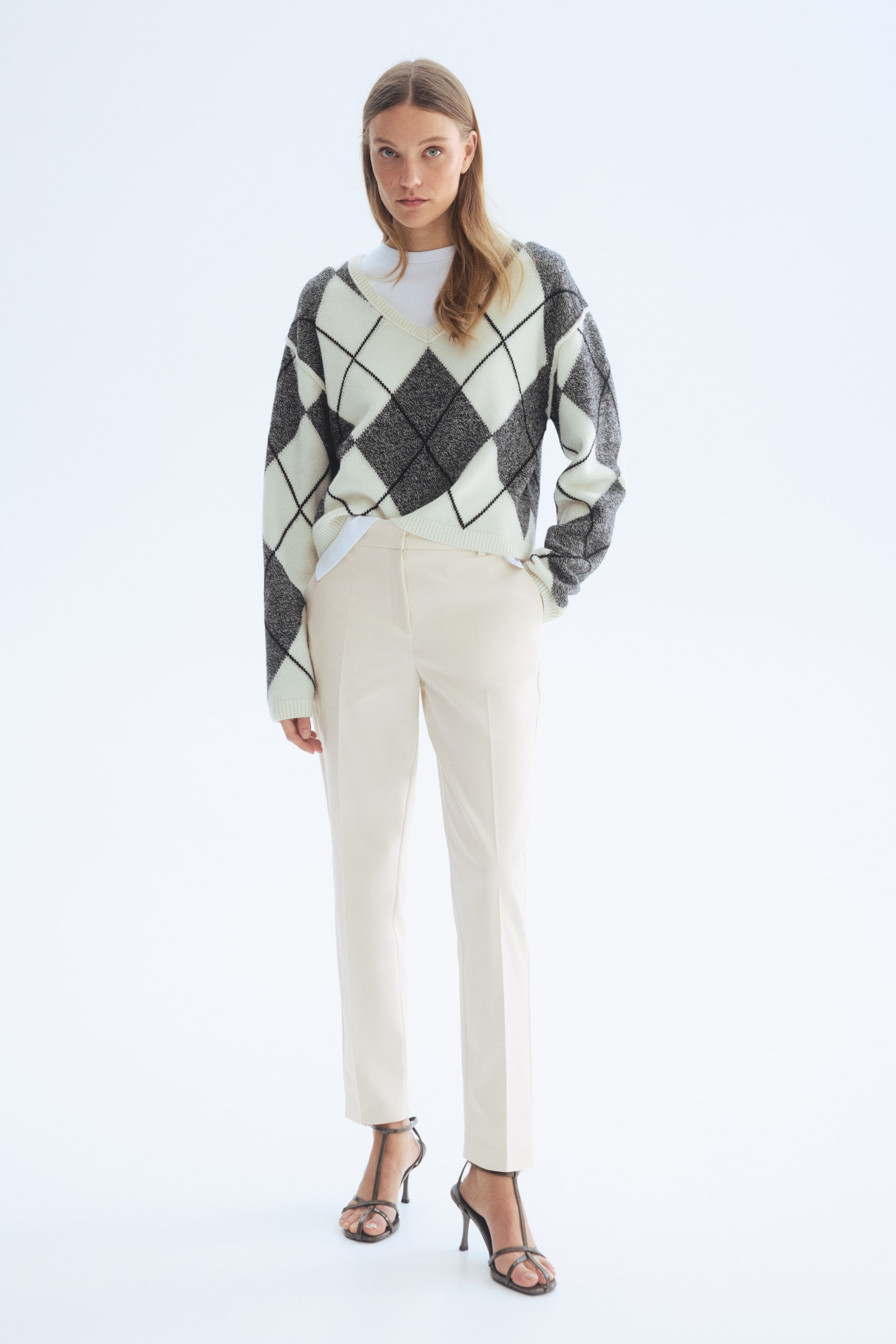 View larger image: An argyle knit jumper featuring a V-neckline and long sleeves. It showcases a pattern of black and white diamonds, with some diamonds filled in mottled grey, layered over a white shirt.