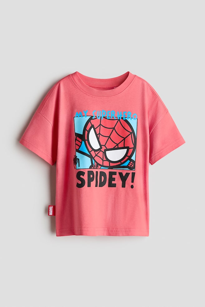 A pink loose-fit t-shirt is presented from the front, showcasing a round, rib-trimmed neckline and dropped shoulders. It displays a graphic print on the chest, featuring a stylised Spider-Man face within a blue square, with the words 'MY SUPER HERO' above and 'SPIDEY!' below. - 1
