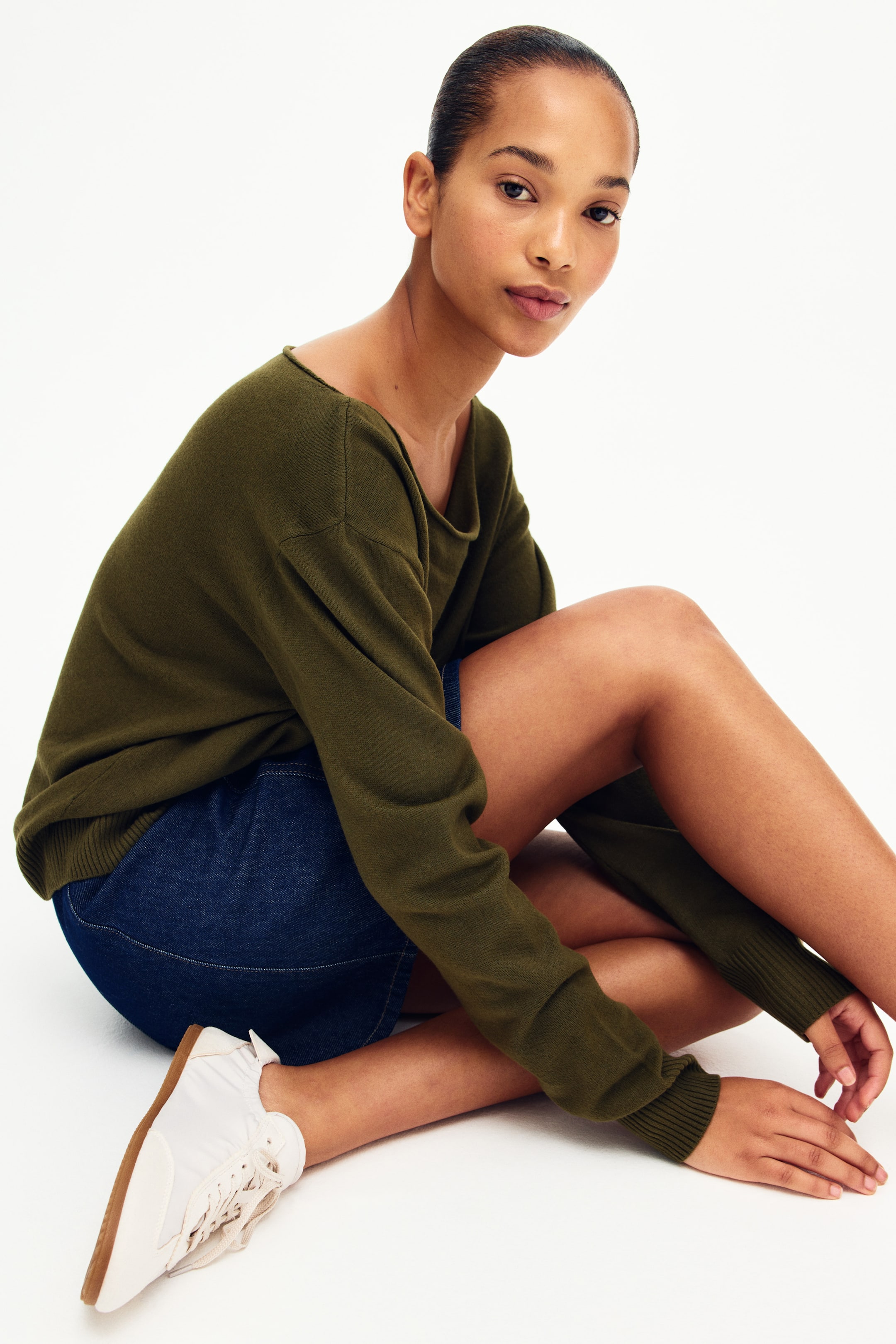 Xem ảnh lớn hơn: Chiếc áo len màu xanh ô liu có cổ thuyền rộng, hơi trễ vai và tay dài kết thúc bằng cổ tay áo bo gân. Trang phục có dáng rộng rãi, thả lỏng quanh thân và cánh tay.