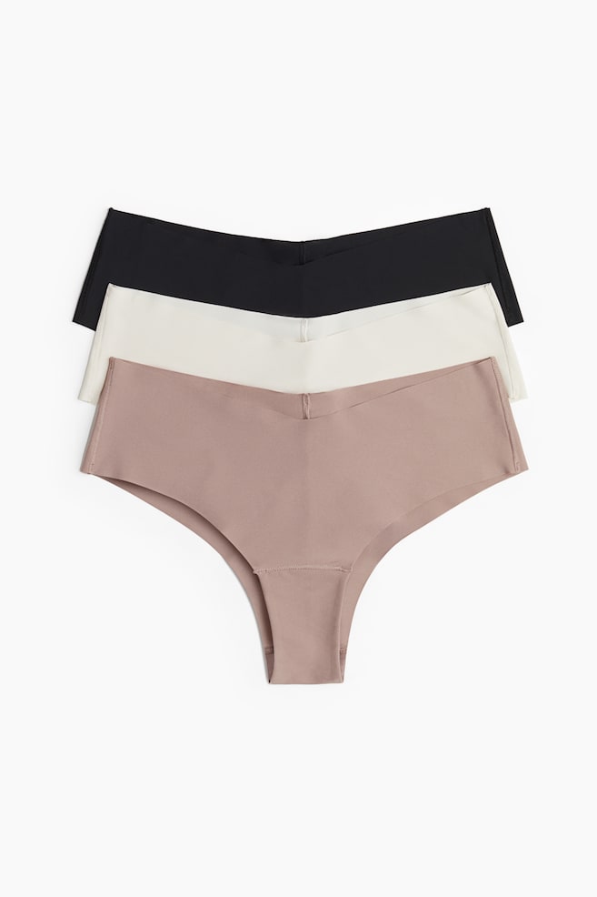 Three microfibre briefs are displayed, stacked and fanned out, showcasing their fronts. The briefs, in black, off-white, and light brown, are each featuring a mid, V-shaped waist and seamless, laser-cut edges. - 1