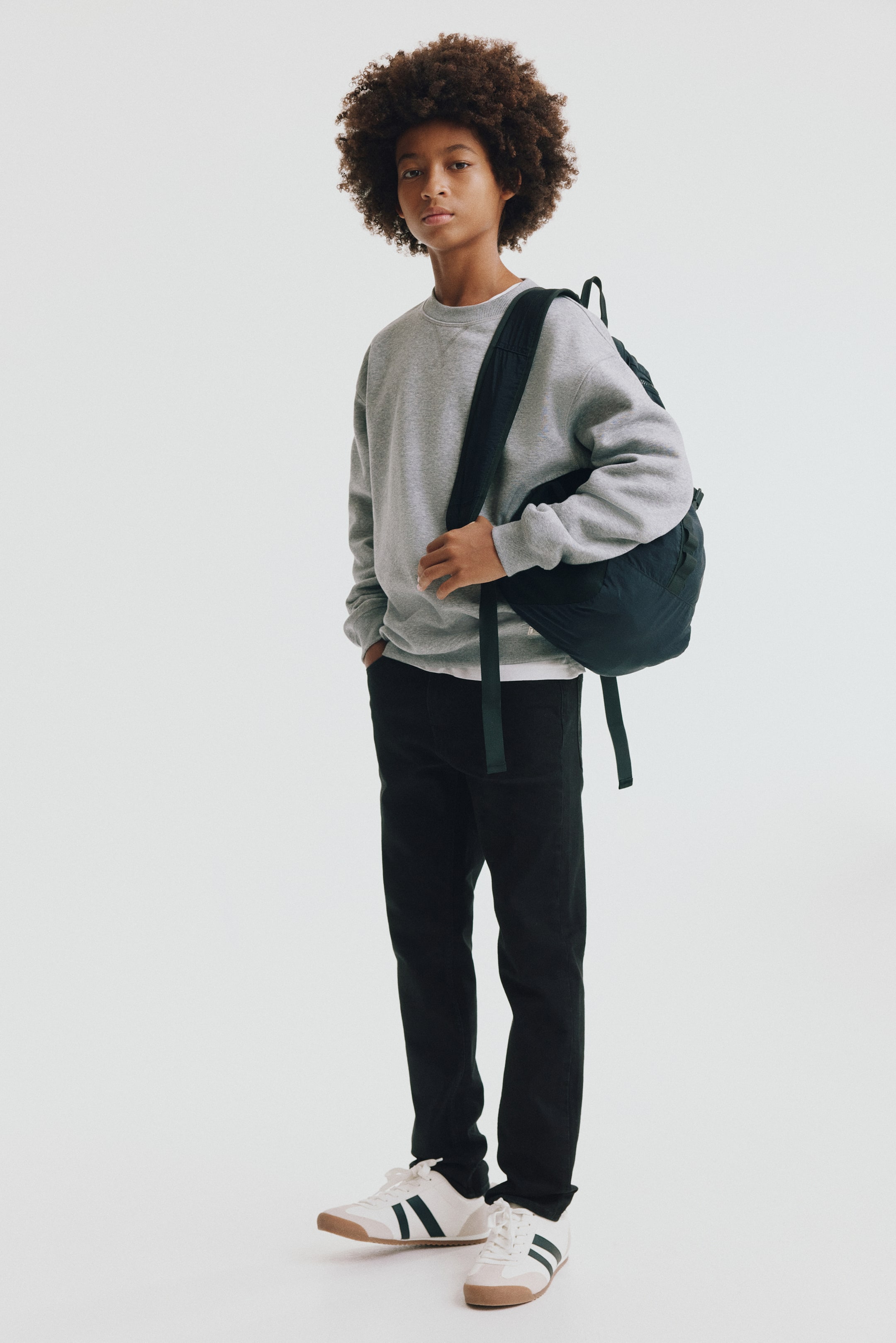 Se større billede: Slim-fit sorte jeans i vasket denim vises forfra på en stående model og har en lige ben-silhuet med lige buksekanter. Jeansene er stylet med en grå sweatshirt, der overlapper taljen, og hvide sneakers.