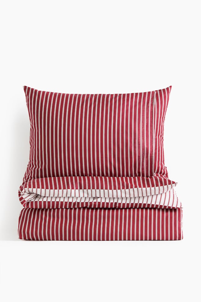 A bedding set featuring a red and white vertically striped pattern is displaying a pillowcase standing upright behind a neatly folded duvet cover, facing front. The folded edge of the duvet cover is revealing a contrasting white stripe pattern along its hem. - 1