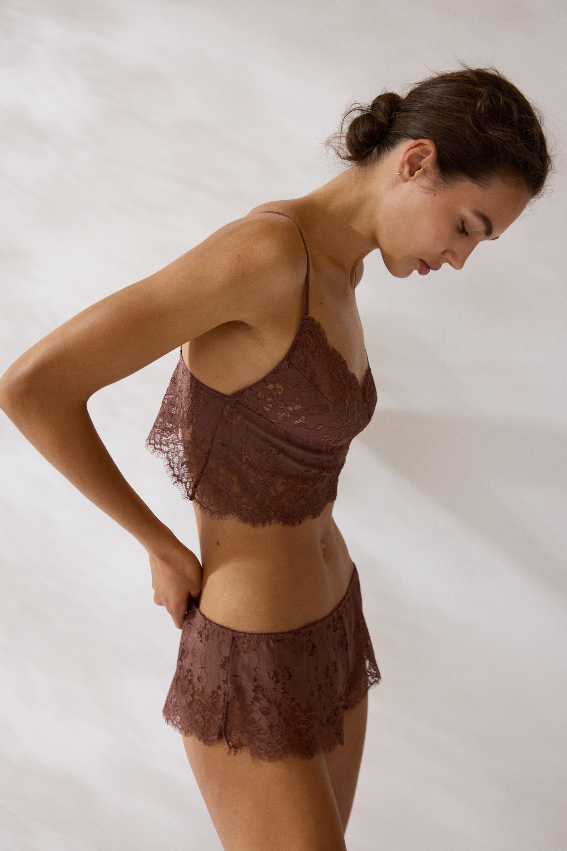 Se større billede: En brun blonde bralette og matchende blonde shorts præsenteres fra en sideprofil. Braletten har tynde spaghetti-stropper, en bølget V-udskæring og en kort længde, mens shortsene fremviser et rynket design med bølgede benåbninger.