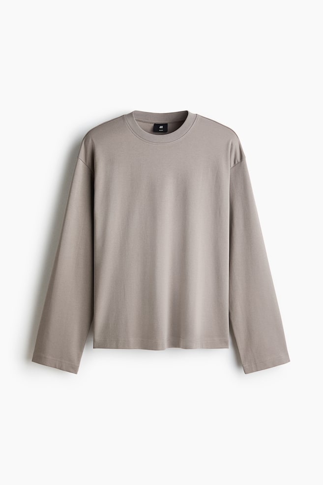 A taupe long-sleeved t-shirt is lying flat, featuring a crew neck, dropped shoulders, wide sleeves, and a straight hem. - 1