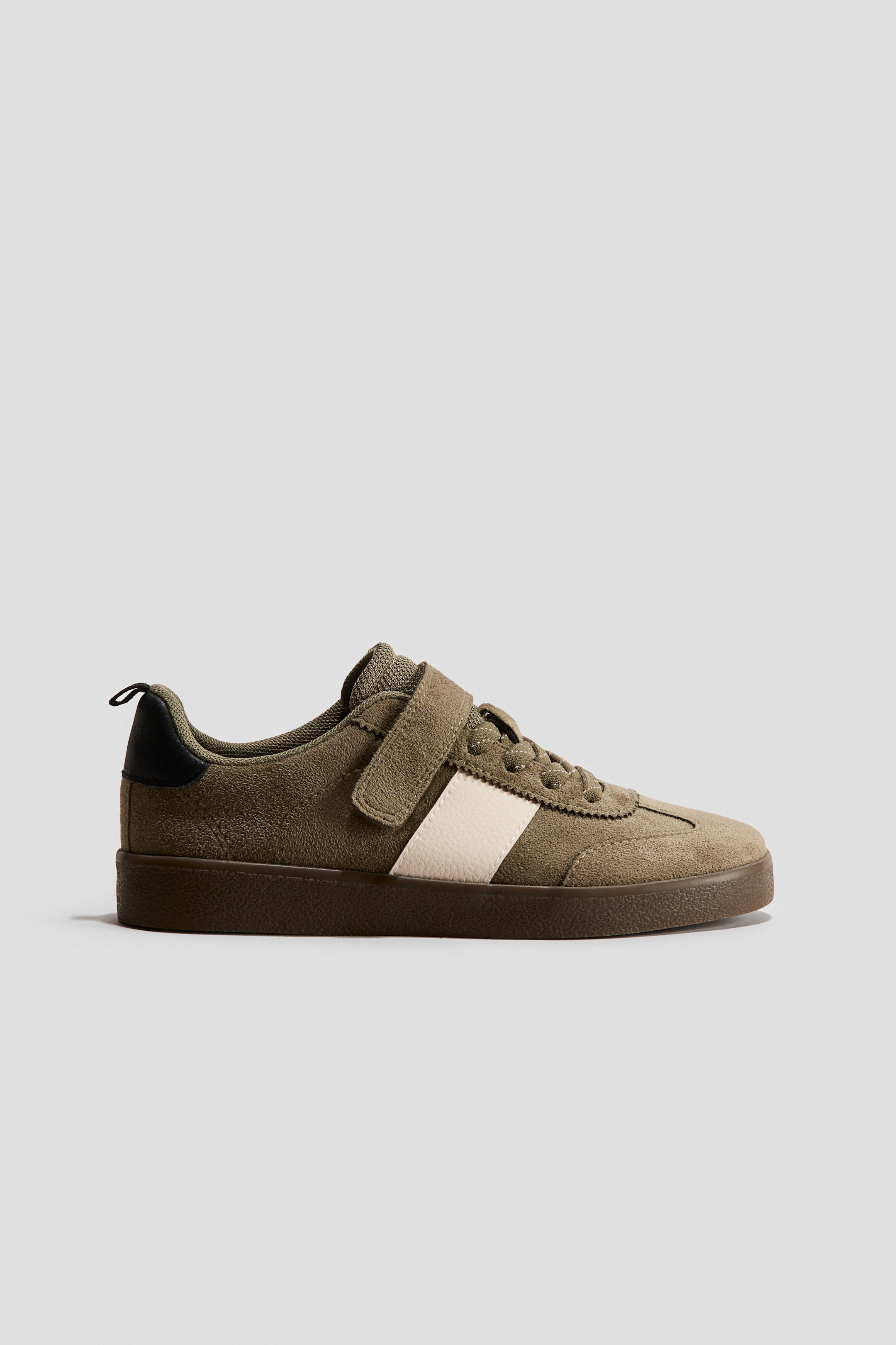 View larger image: Sneakers. The olive green suede sneaker features a cream stripe on the side, a hook-and-loop strap, and a dark brown sole. A black pull tab is visible at the heel.