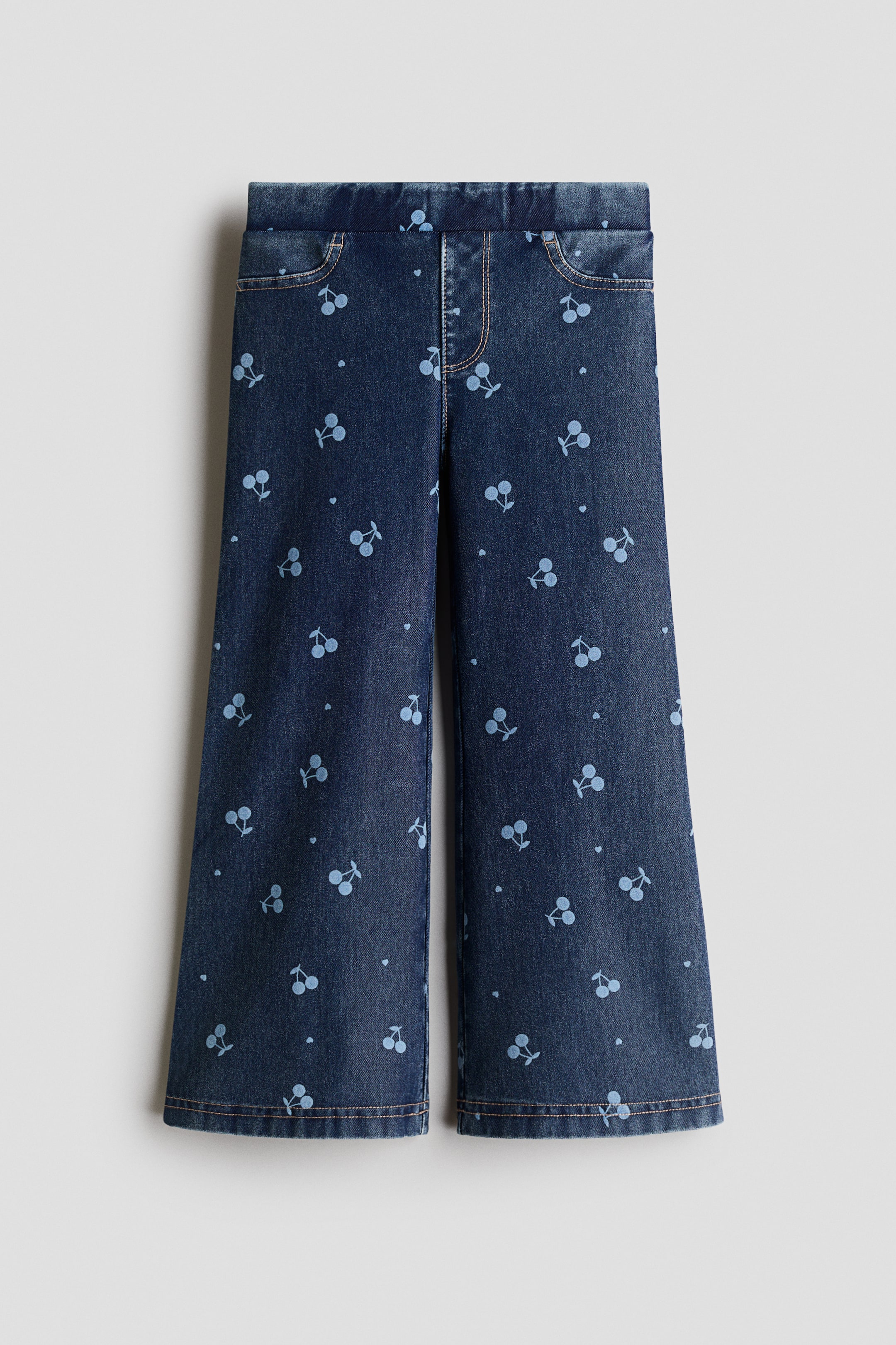 View larger image: The pants showcase a dark blue denim-like fabric adorned with a light blue cherry and heart print throughout, offering a front view. They are crafted with an elasticated waistband, stitched curved pockets, and a wide-leg silhouette with stitched hems.