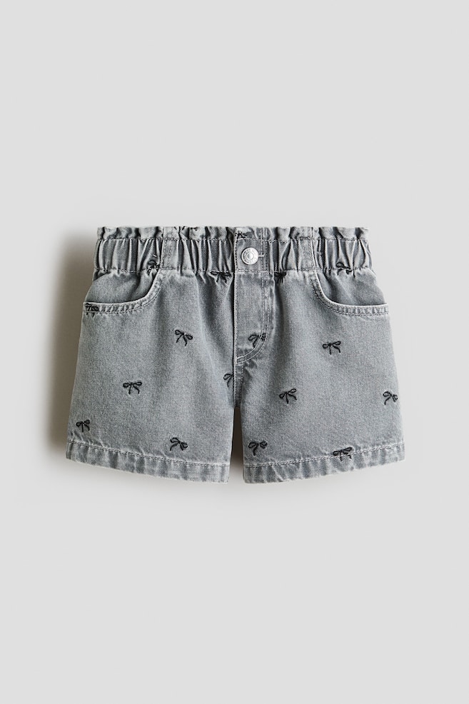 These grey cotton-weave shorts are shown from the front, featuring an elasticated paperbag waist and scattered black embroidered bows. The shorts are displaying a mock fly with a silver press stud and two curved front pockets. - 1