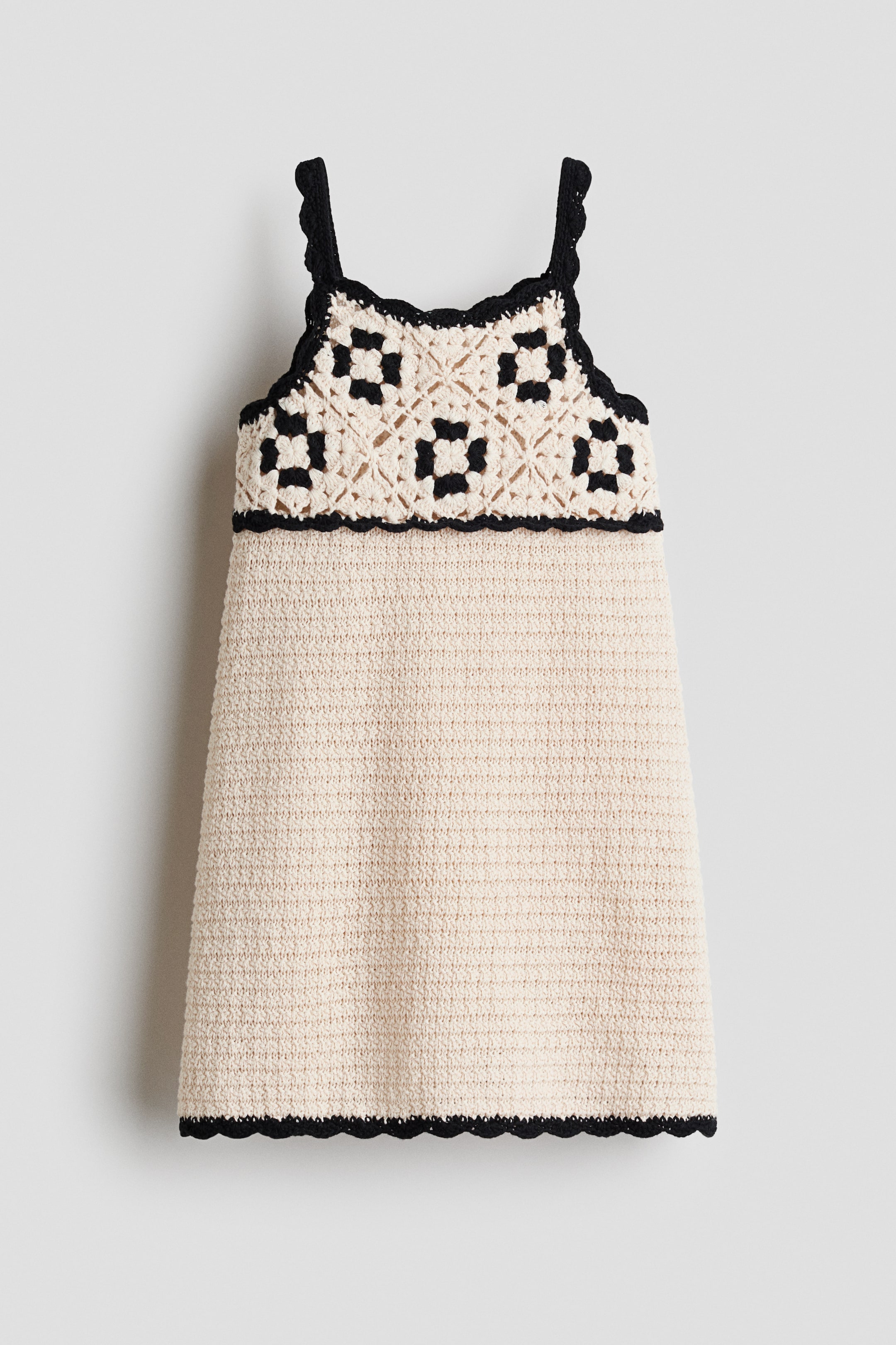 Größeres Bild ansehen: Ein Kleid aus gestrickter Baumwolle mit Häkeloptik ist von vorne sichtbar. Es verfügt über kontrastierende schwarze Details und gewellte Kanten, einen quadratischen Ausschnitt, schmale Träger und einen sanft ausgestellten Rock.