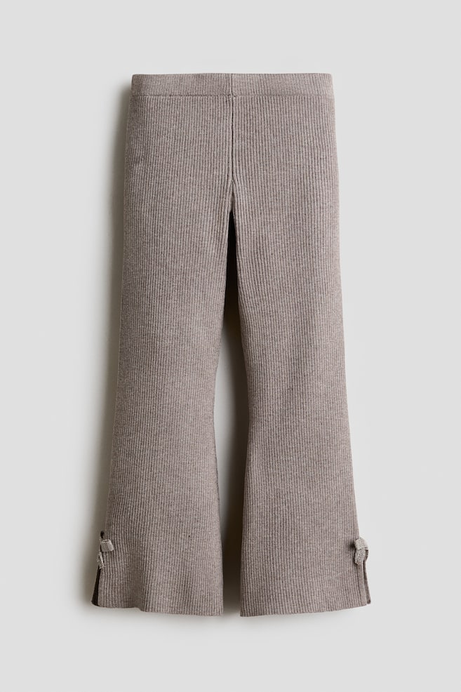 Diese gerippten Leggings in Taupe-Braun werden von vorne gezeigt und verfÃ¼gen Ã¼ber einen elastischen Bund sowie eine dichte, vertikale Rippstruktur. Die Beine sind zum Saum hin ausgestellt und zeigen seitliche Schlitze an den Ã¤uÃeren KnÃ¶cheln, die mit kleinen dekorativen Knoten akzentuiert sind. - 1