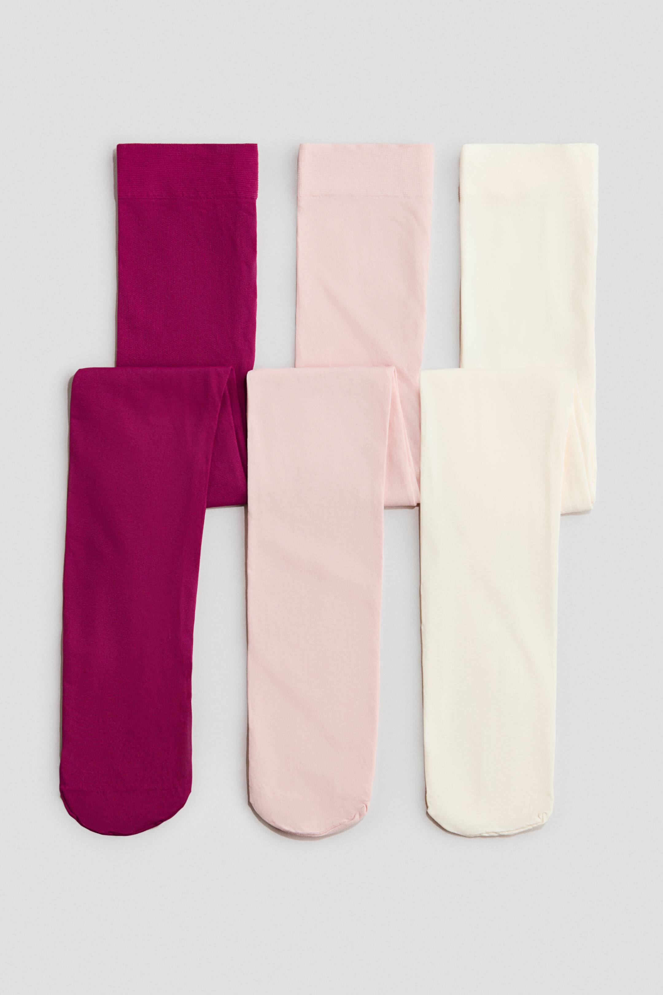 Zobacz większy obraz: Sześć par cienkich rajstop z elastycznym pasem leży złożonych. Elastyczne pasy są skierowane do PRZODU, a rajstopy występują w kolorach magenta, jasnoróżowym i kremowym, z dwoma parami każdego koloru ułożonymi w dwóch rzędach.