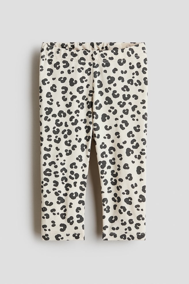 "Leggings in a soft, cream-coloured cotton jersey showcase a front view, featuring a black leopard print pattern and an elasticated waist." - 1