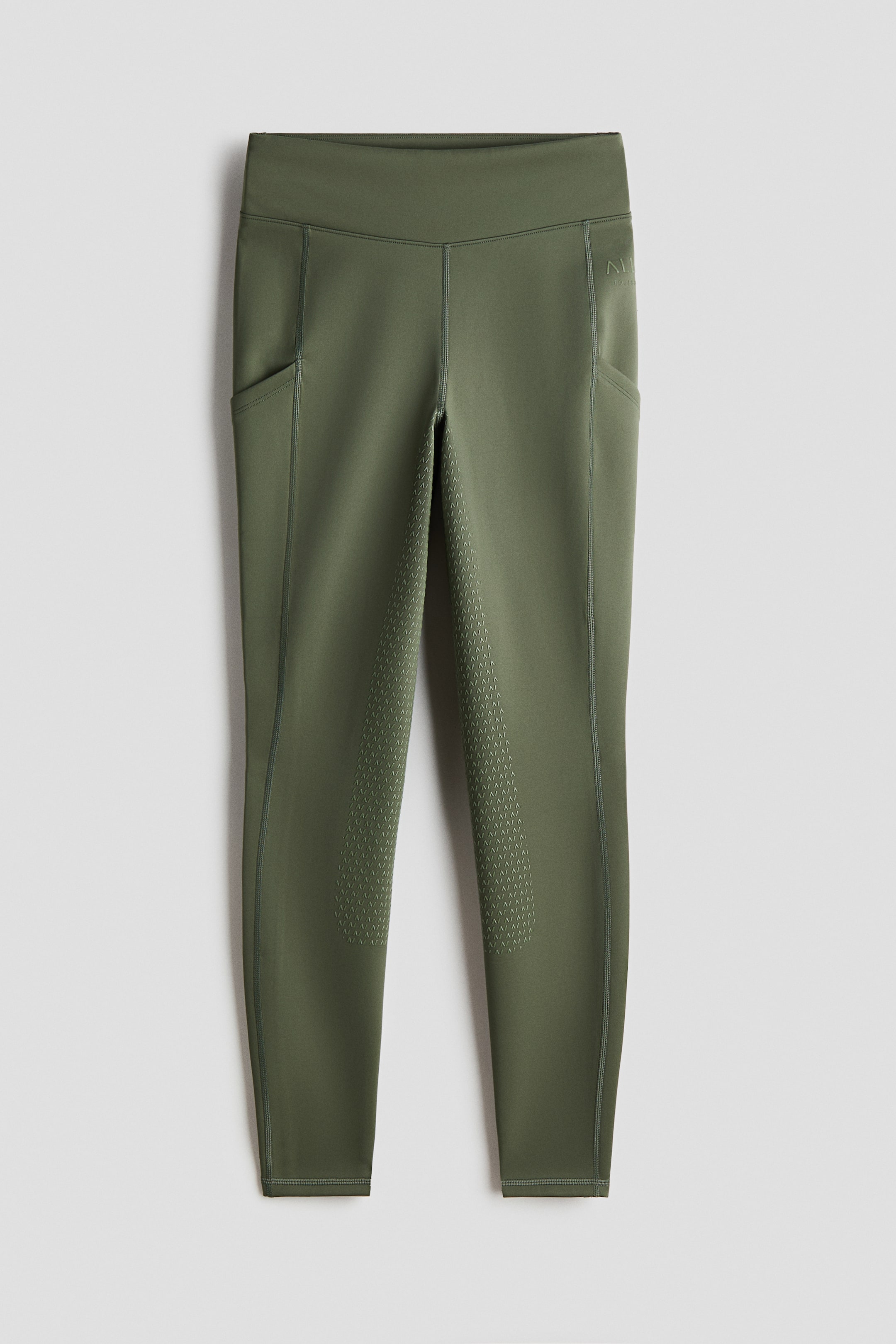 View larger image: Riding leggings — front view, in a solid olive green colour, featuring a high waist with a wide waistband and integrated side pockets on both thighs. A full silicone grip pattern covers the inner thighs and knees.