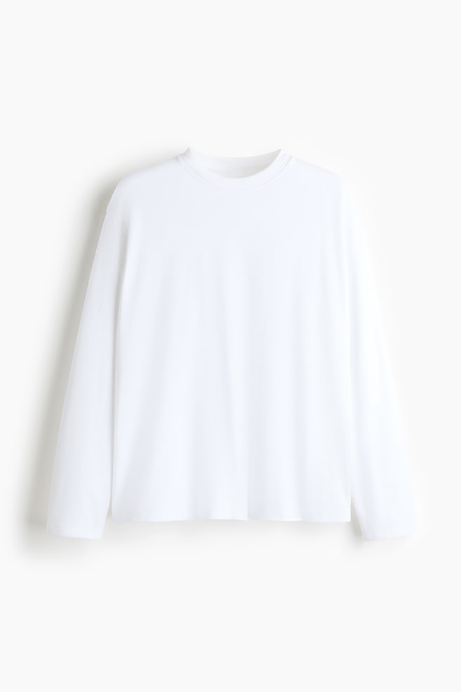 A white, relaxed-fit long-sleeve t-shirt is hanging in a front view, showcasing a round neckline, long sleeves, and a straight-cut hem. - 1