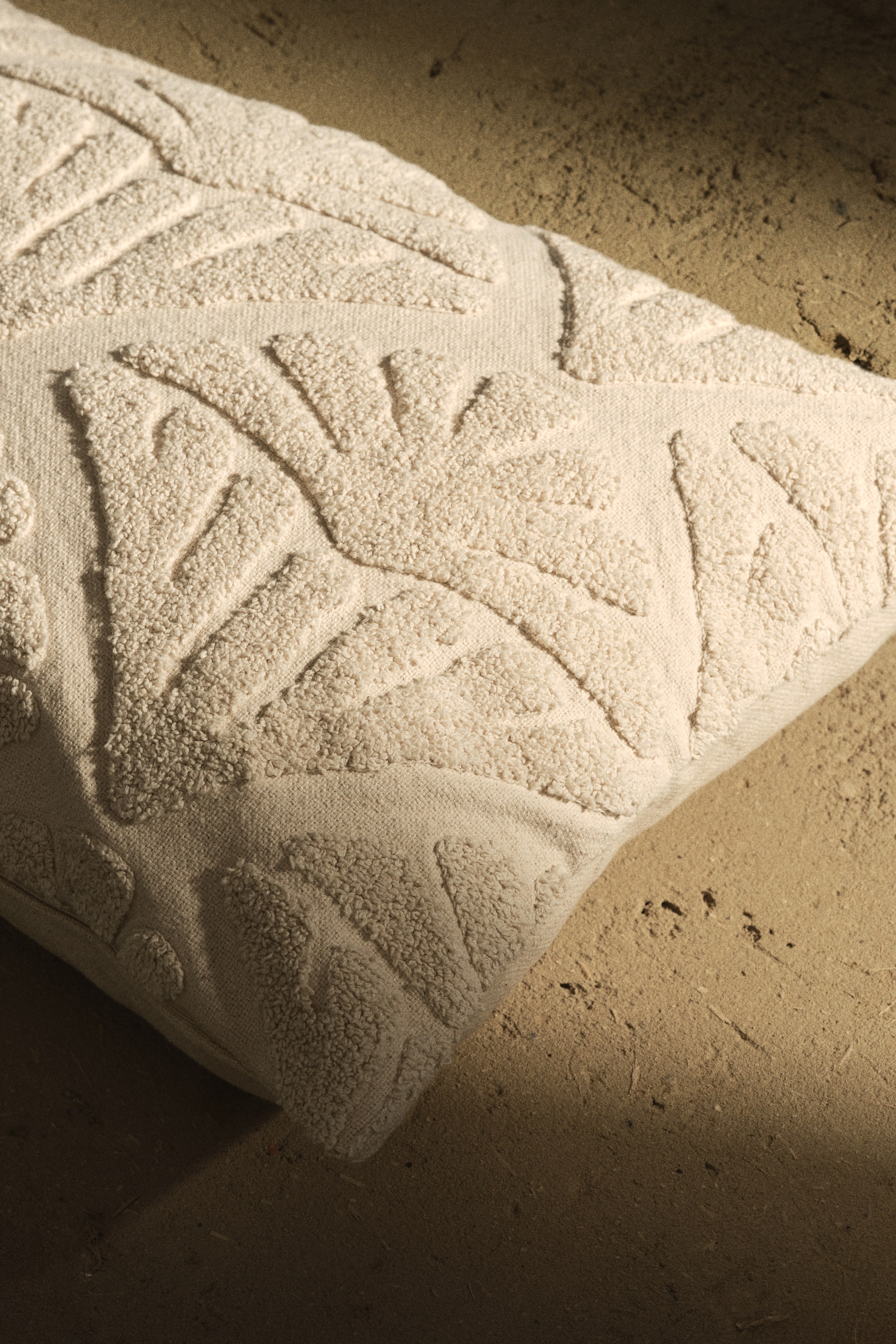 View larger image: A cream-colored rectangular pillow is placed diagonally, featuring a raised, tufted botanical pattern across its top surface.