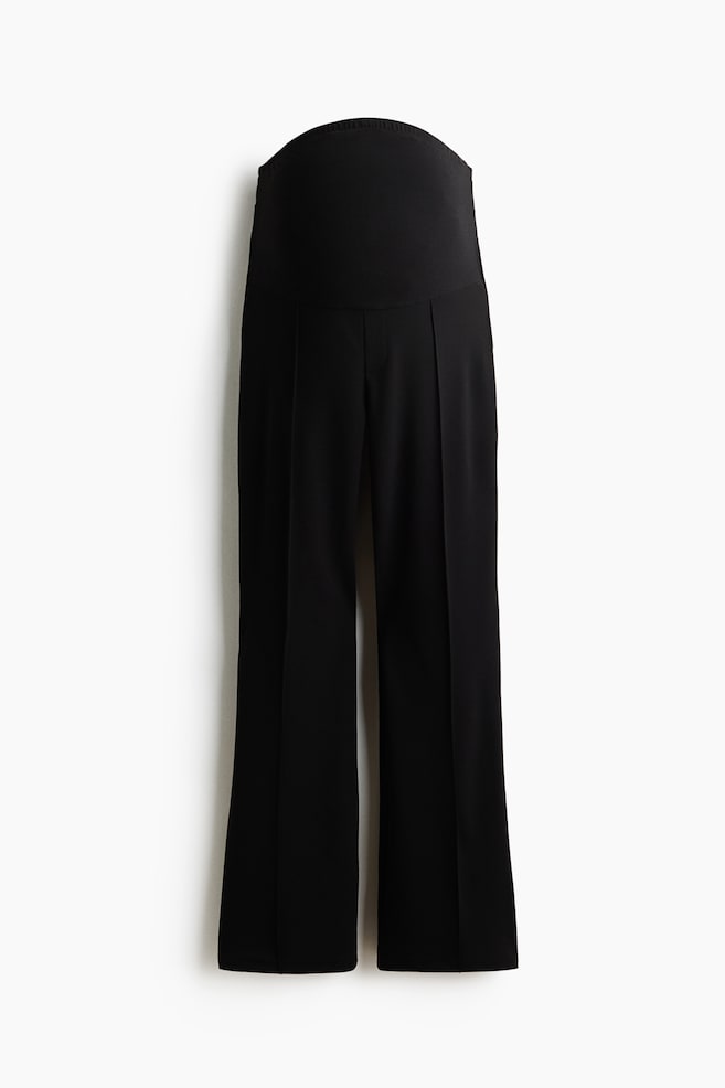 A pair of black wide-leg maternity trousers is shown from the front, featuring a high, elasticated over-the-bump waistband. The trousers are displaying sharp pressed creases running down the center of each leg. - 1