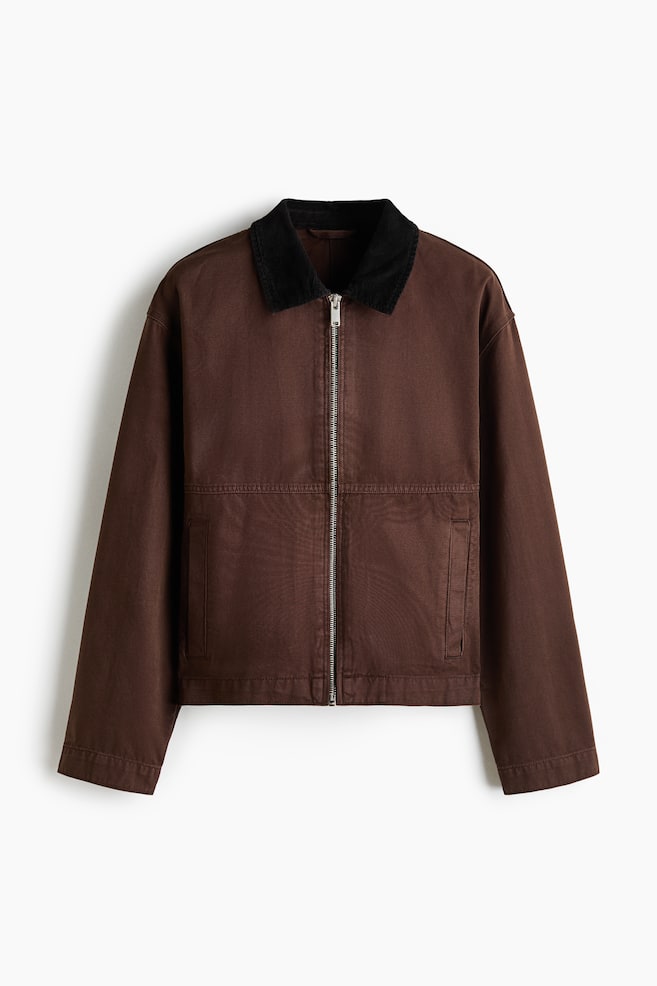 Eine kurze Arbeitsjacke aus braunem Baumwoll-Canvas wird von vorne präsentiert und zeichnet sich durch einen kontrastierenden schwarzen Cordkragen aus. Ein silberfarbener Reißverschluss verläuft entlang der Vorderseite, mit zwei Leistentaschen vorne, langen Ärmeln und einem geraden Saum, die das Design vervollständigen. - 1