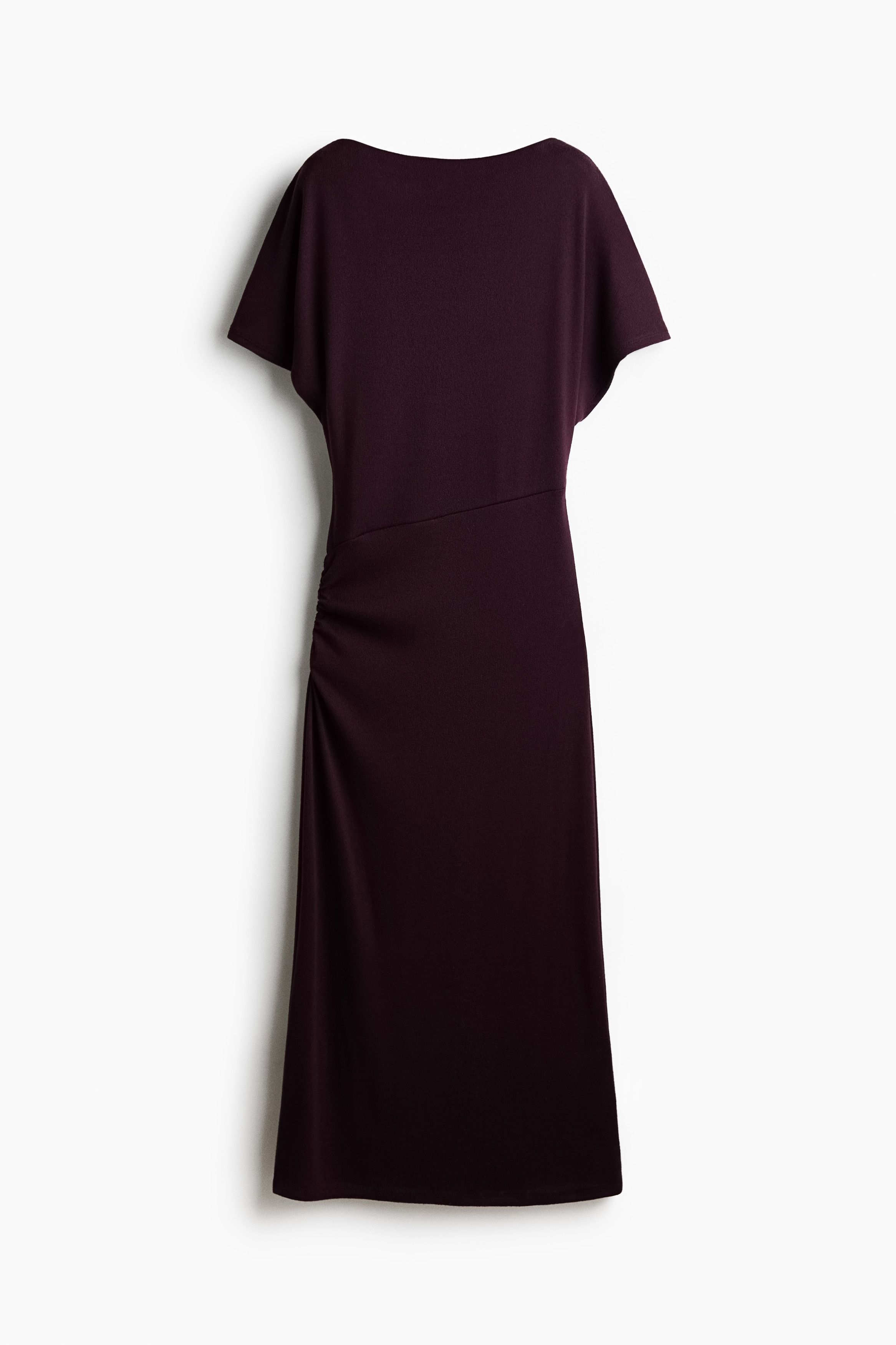 A dark burgundy knitted dress featuring a boat neck, a loose-fit bodice, and short butterfly sleeves is being worn by the model. The dress showcases a diagonal seam at the waist and gathers at the hips, where the model is resting her hands.