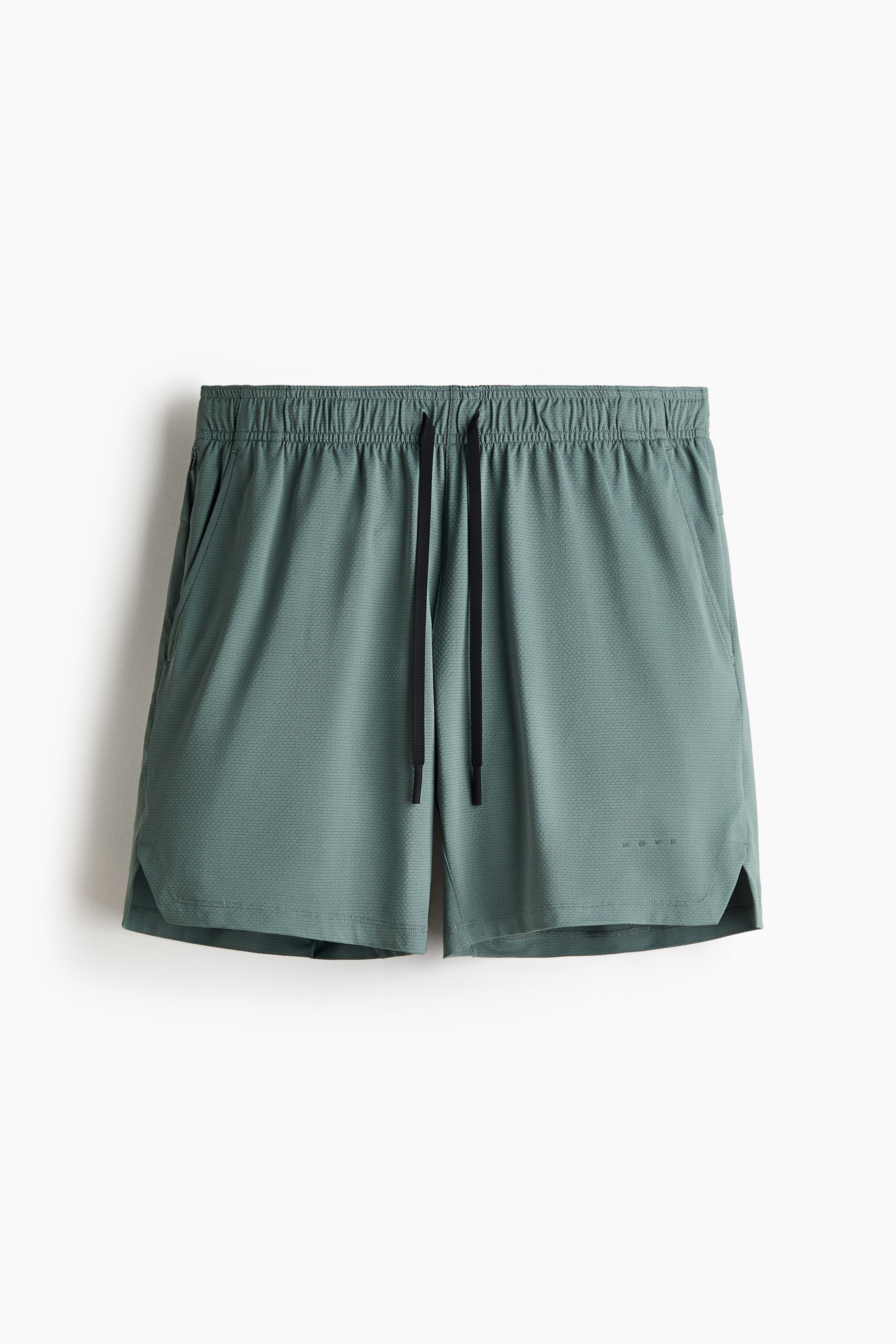 View larger image: Dusty green sports shorts are showcased from the front, highlighting an elasticated waistband with black drawstrings, side pockets, and a subtly textured fabric. Small slits adorn the side hems, complemented by "MOVE" branding on the lower right leg.