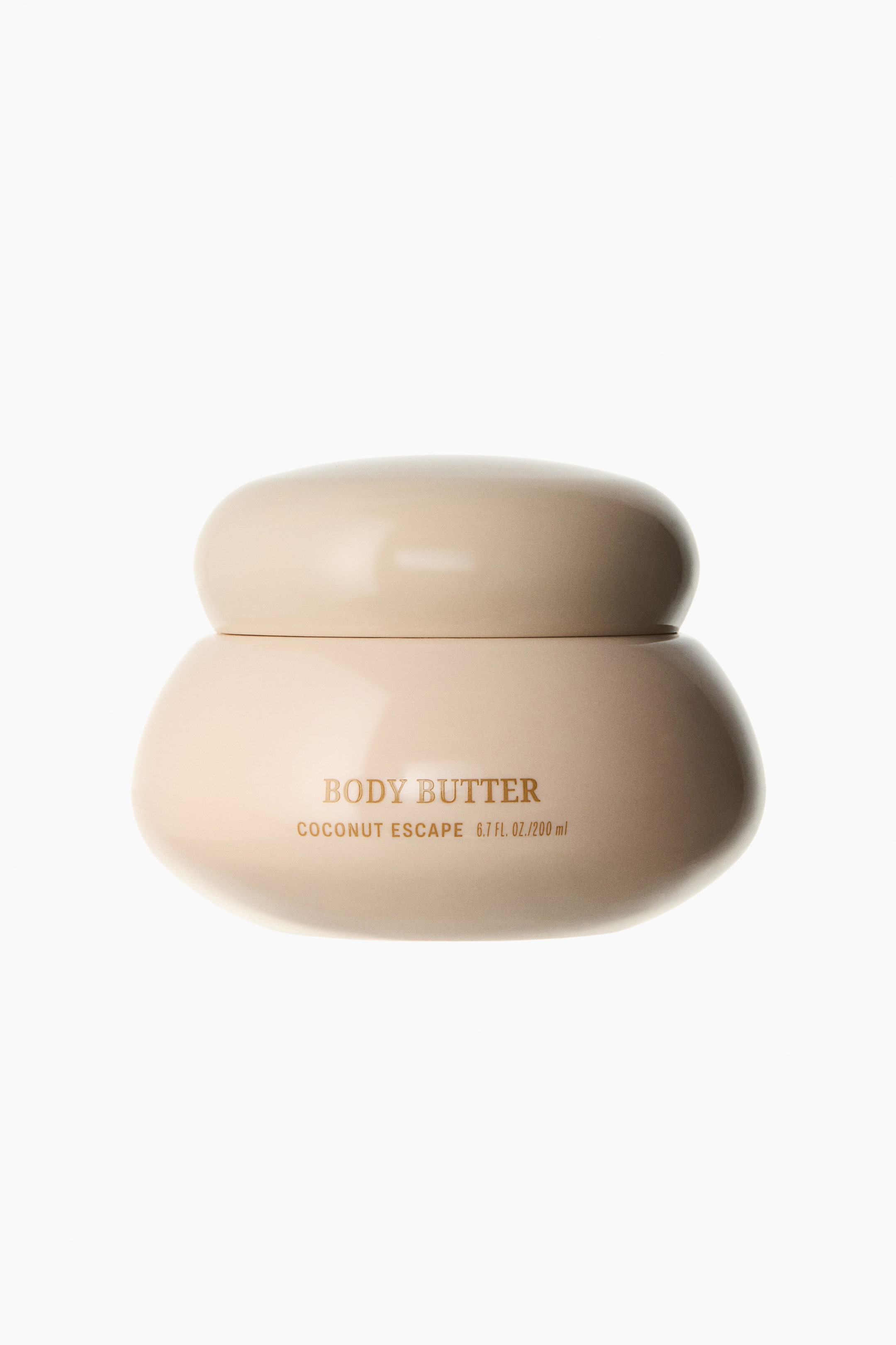 View larger image: A light beige body butter jar is showcased facing forward, featuring a rounded, pebble-like design with a matching lid. Gold lettering on the front of the jar reads 'BODY BUTTER' and 'COCONUT ESCAPE 6.7 FL. OZ./200 ml.'