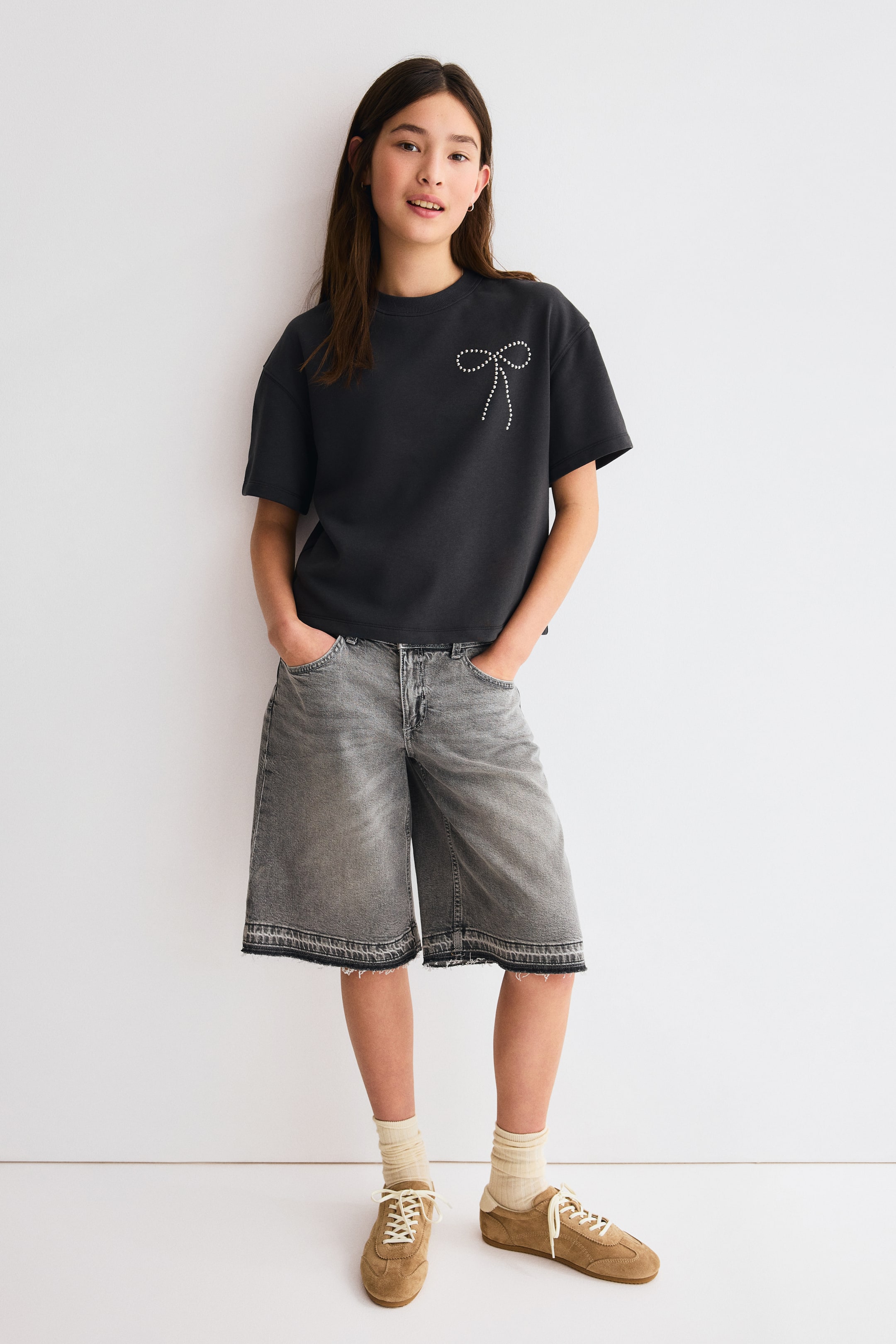 View larger image: An oversized black t-shirt showcases a bow design crafted from small white studs on the left chest. It offers a relaxed fit with short sleeves and a round neckline.