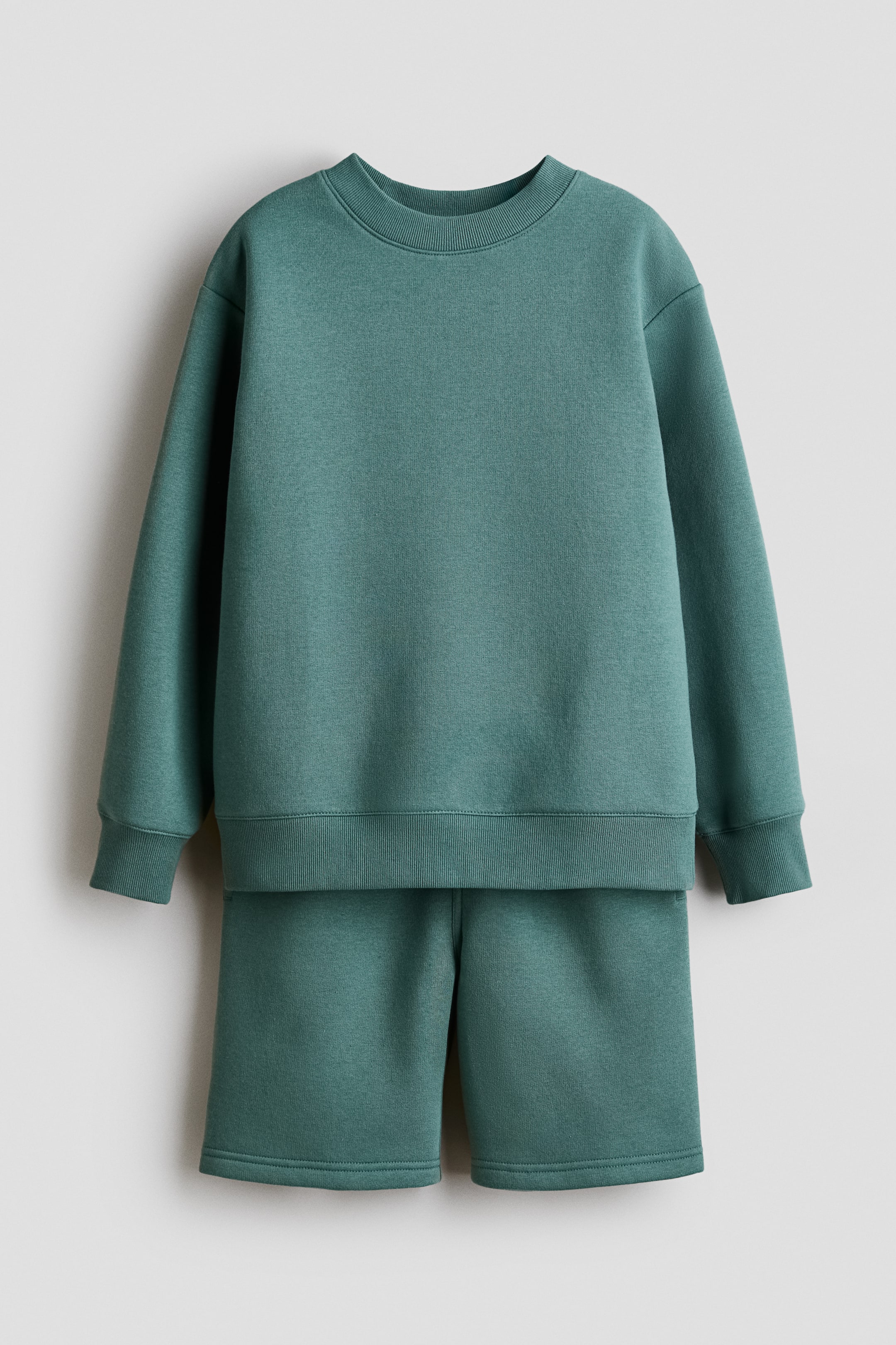 Se større billede: Et teal matchende sæt består af en langærmet top med en rund, ribbet halsudskæring, ribbede manchetter og en ribbet kant. De medfølgende shorts har en glat talje og en flad kant.