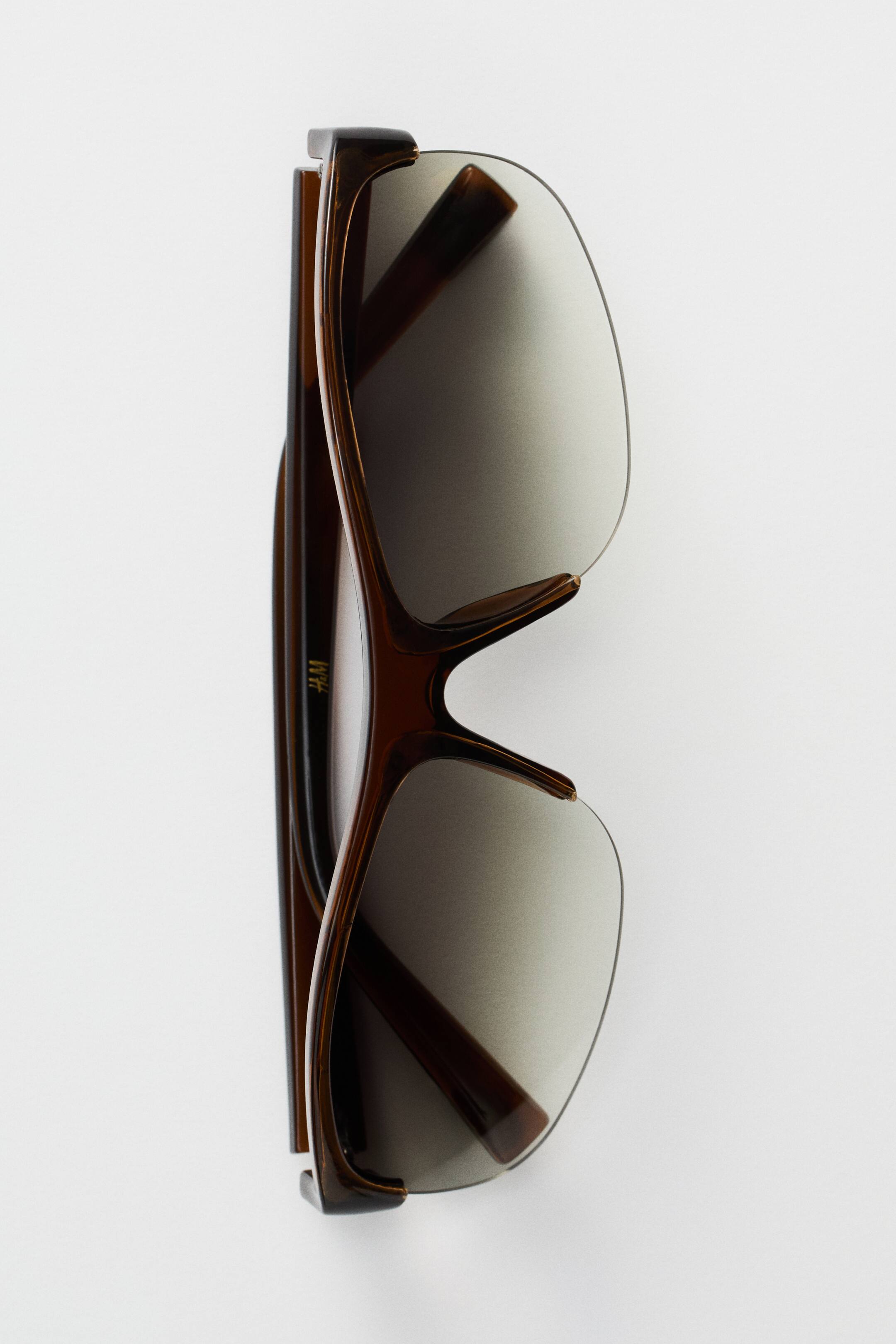 View larger image: Sporty sunglasses featuring a brown plastic half-frame with plastic sidepieces and tinted, UV-protective plastic lenses, presented with the sidepieces folded inward.
