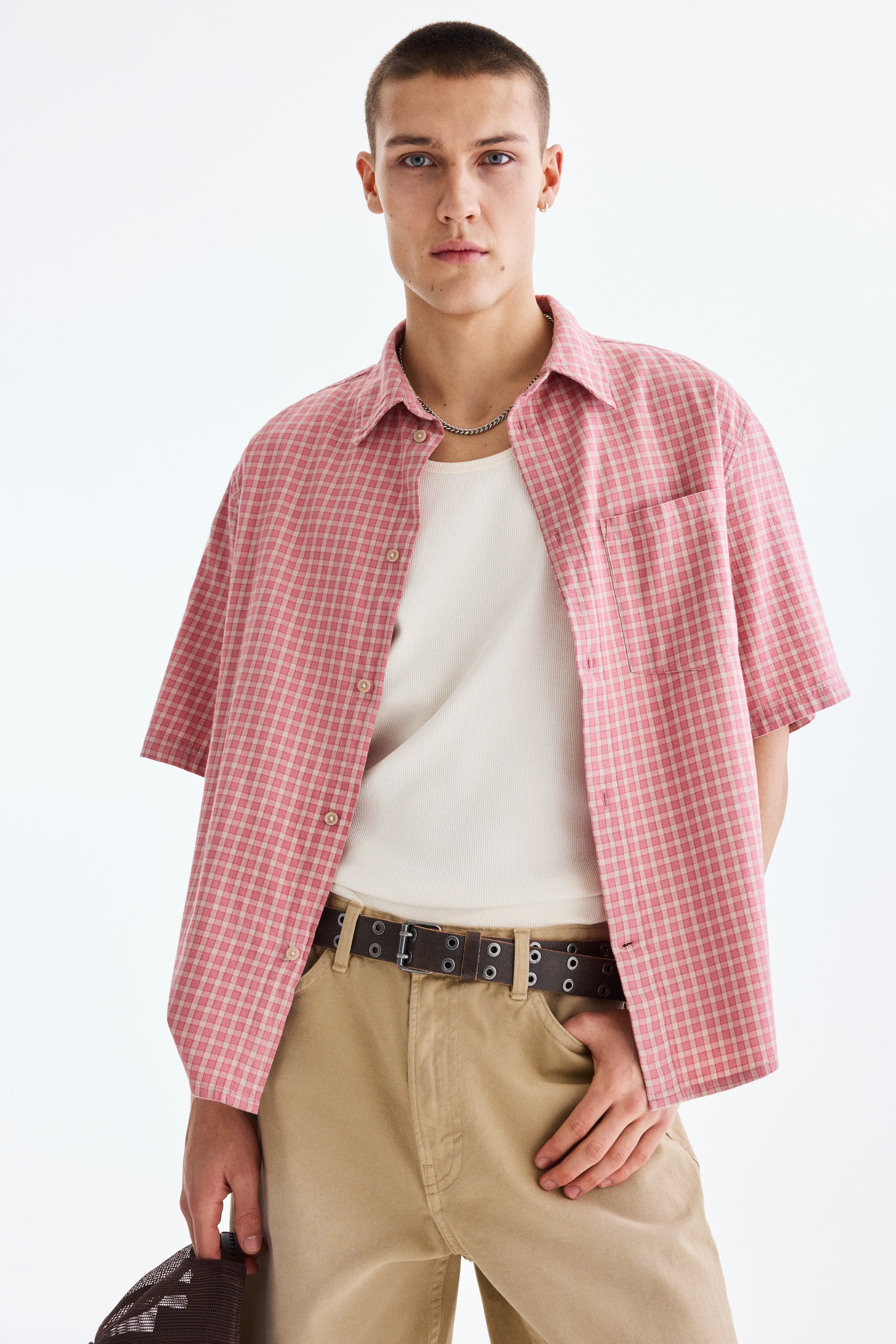 View larger image: A pink plaid short-sleeved shirt featuring a pointed collar and a single chest pocket on the left side. It's worn open over a white ribbed tank top, offering a relaxed fit.