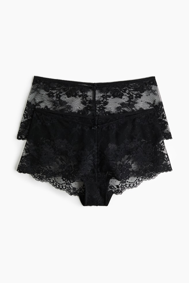 A two-pack of black lace boyshort panties is resting flat, with one pair layered slightly behind the other to display the front design. Both pairs are featuring an all-over sheer floral lace pattern, scalloped hemlines along the leg openings, and a small decorative button at the center of the waistband. - 1