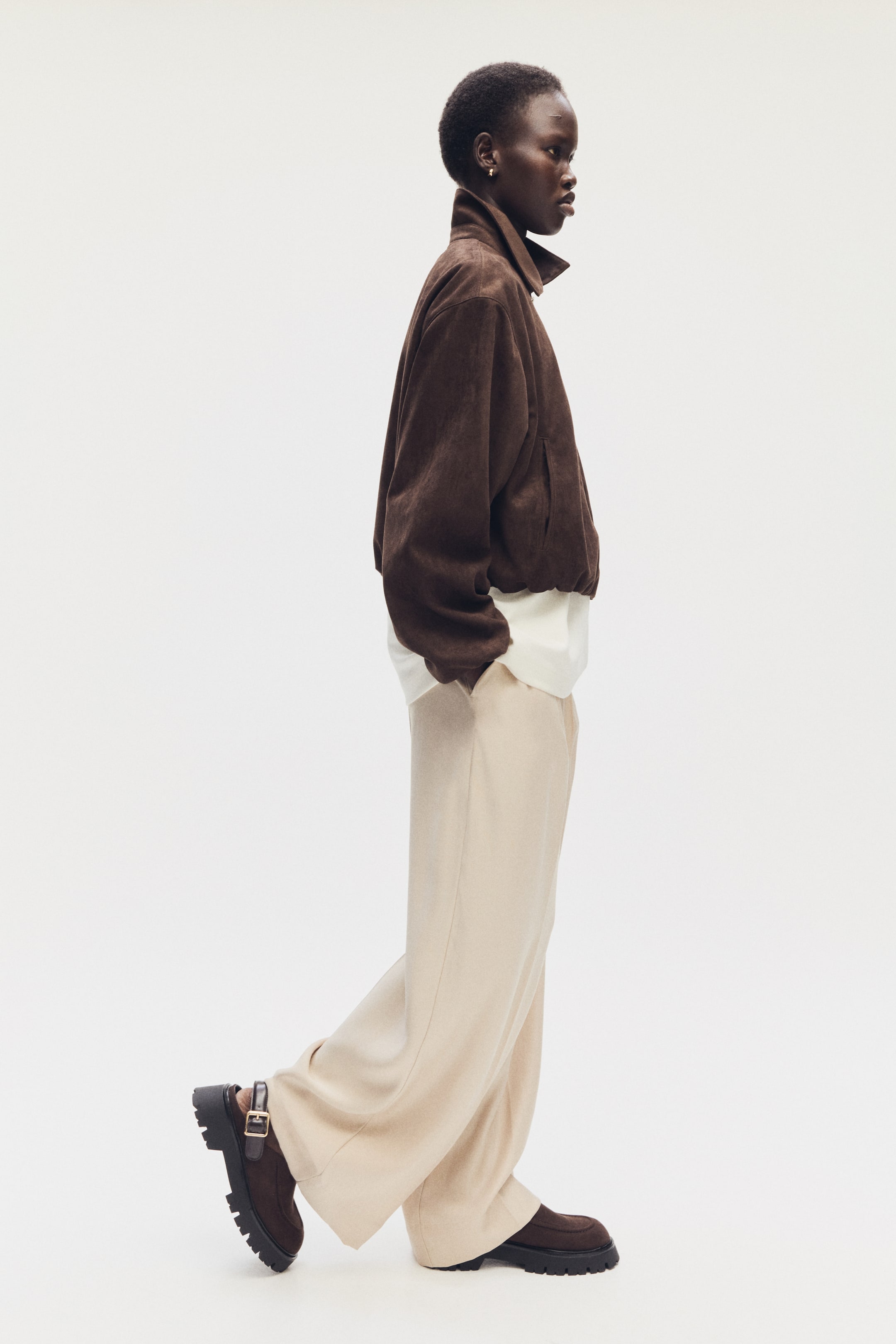 Agrandir l'image: Les mules loafers à bouts arrondis, avec une couture mocassin, une patte réglable ornée d'une boucle en métal à l'avant, et des semelles épaisses et texturées sont portées par le mannequin, qui marche.