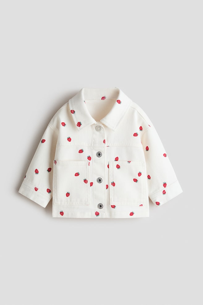 Off-white-värinen takki on kuvattu suoraan edestäpäin. Siinä on kauttaaltaan printti punaisista mansikoista vihreine varsineen. Takissa on klassinen kaulus, edessä nepparikiinnitys hopeansävyisillä napeilla sekä neljä läpällistä päällitaskua. - 1