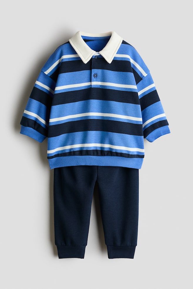 A two-piece set is shown from the front, featuring a striped rugby shirt and solid navy track pants. The long-sleeved shirt features horizontal stripes in light blue, navy, and white, with a contrasting white collar and ribbed trims, while the matching pants have ribbed ankle cuffs. - 1