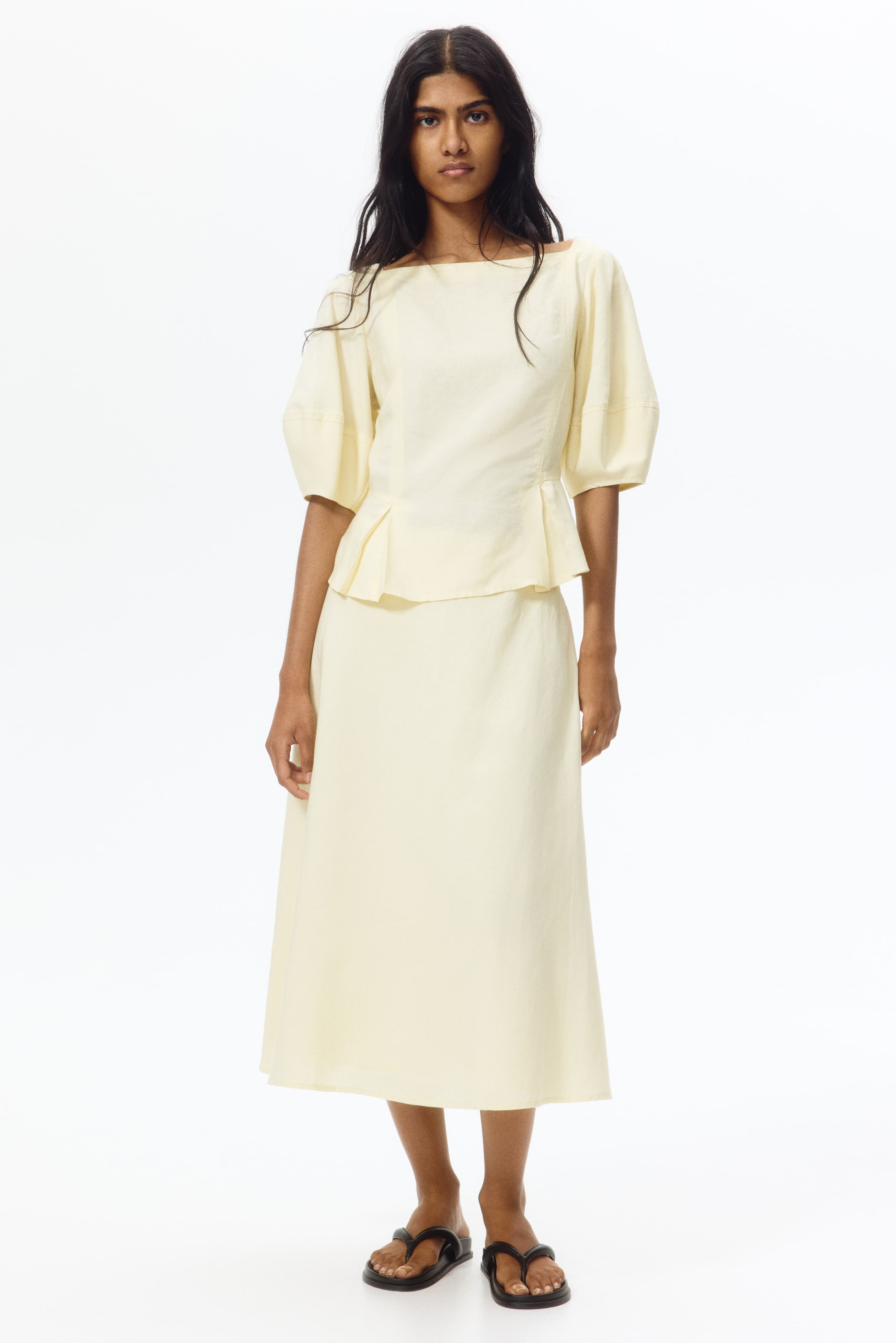View larger image: Presenting a light yellow two-piece set, showcasing a top with a wide boat neckline, elbow-length puffed sleeves, and a pleated peplum hem, complemented by a matching A-line midi skirt.