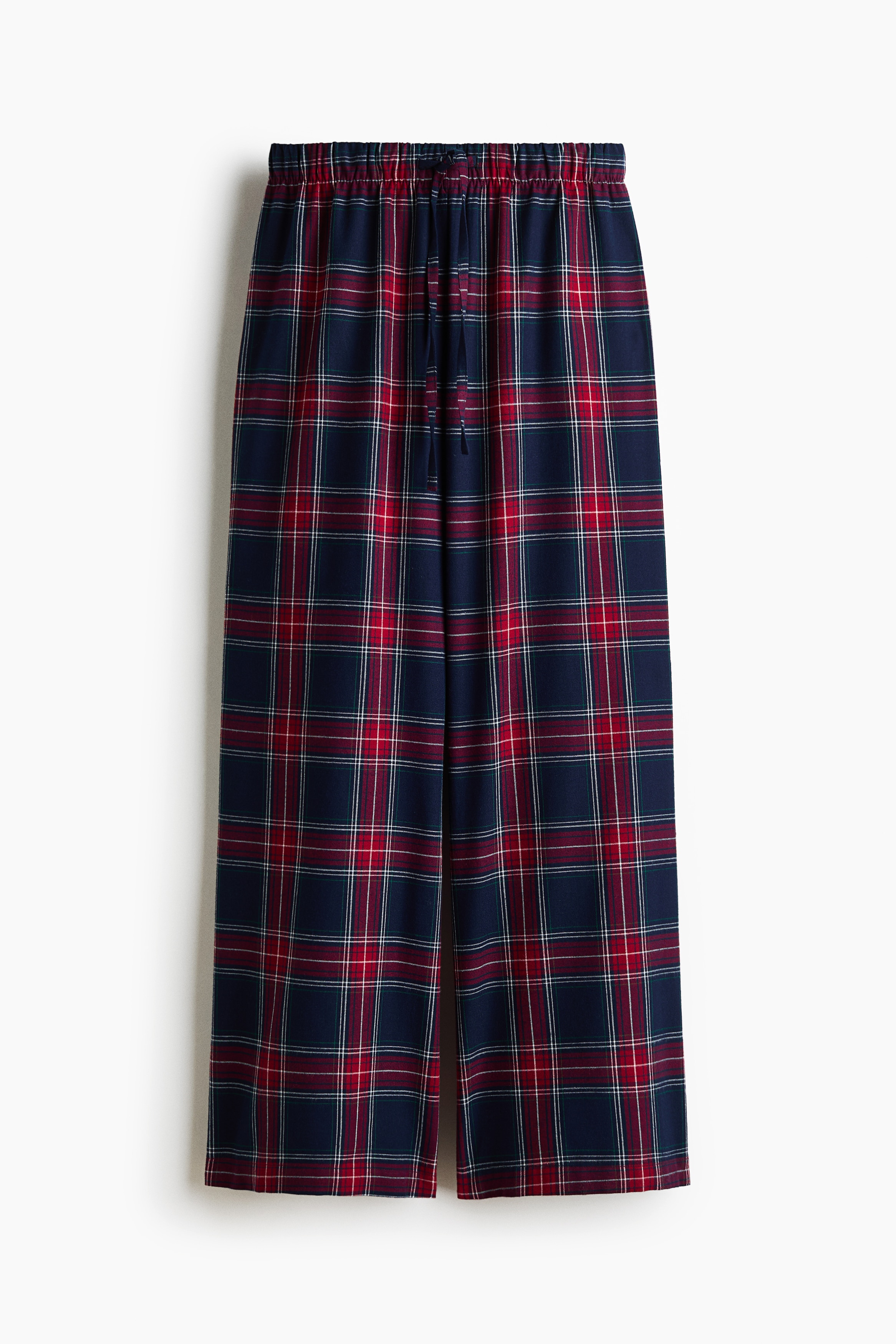 Plaid flannel pyjama pants featuring a red and navy tartan pattern, an elasticated drawstring waist, and wide legs are being worn by the model. The pants are styled with a white bralette.