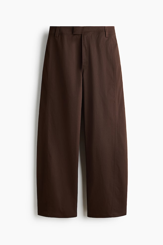 Dunkelbraune Twillhose von vorne gezeigt, mit einer strukturierten Barrel-Leg-Silhouette und markanten, nach vorne verlaufenden SeitennÃ¤hten. Das Design zeigt einen verlÃ¤ngerten Bund mit GÃ¼rtelschlaufen, einen ReiÃverschluss und dezente Seitentaschen. - 1
