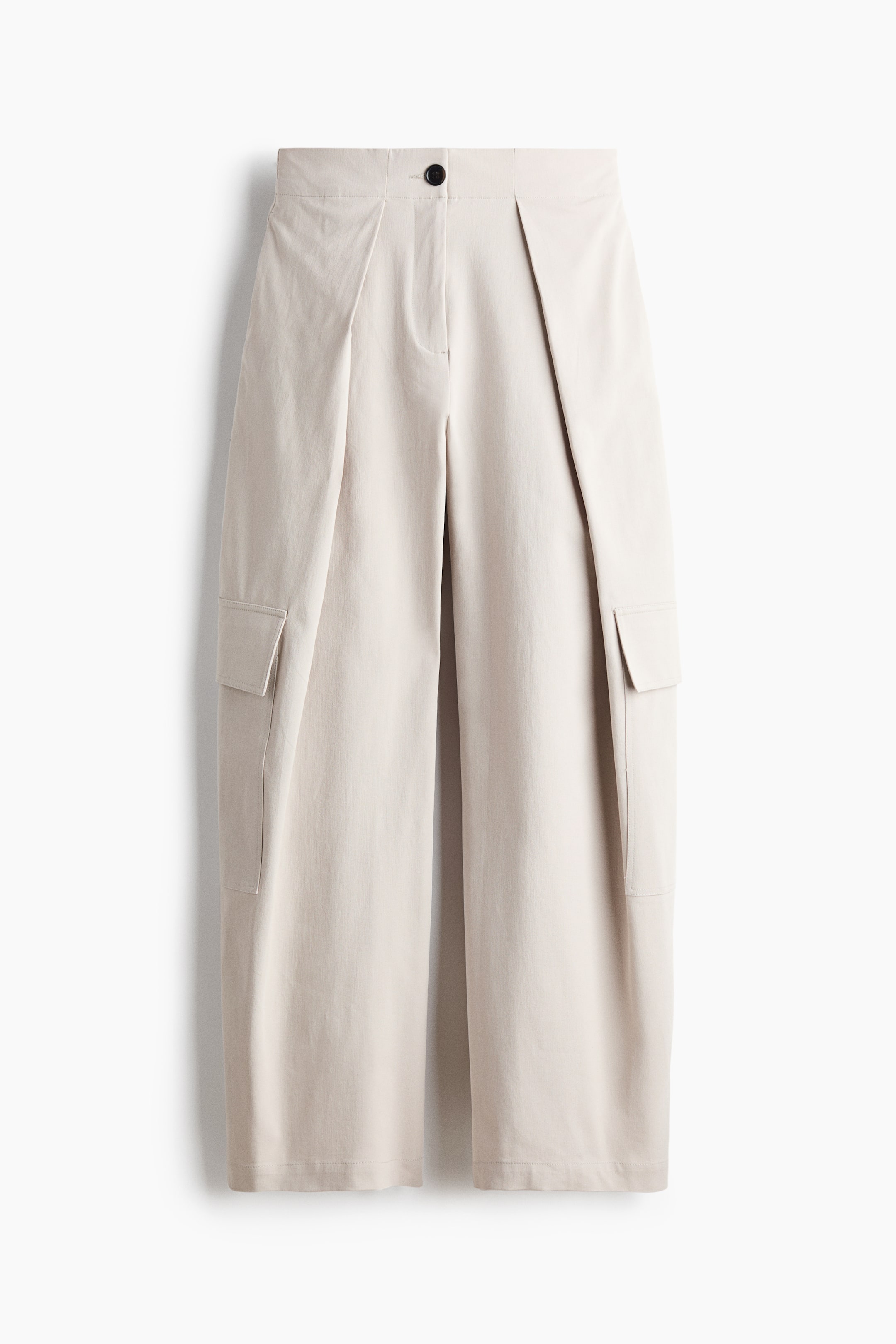 Grotere afbeelding bekijken: Licht beige wijde broek met wijde pijpen, frontaal weergegeven, met een platte tailleband met een zwarte knoopsluiting en opvallende naar voren gerichte plooien die vanaf de taille lopen. Twee klepzakken zijn zichtbaar aan de zijkanten van de benen.