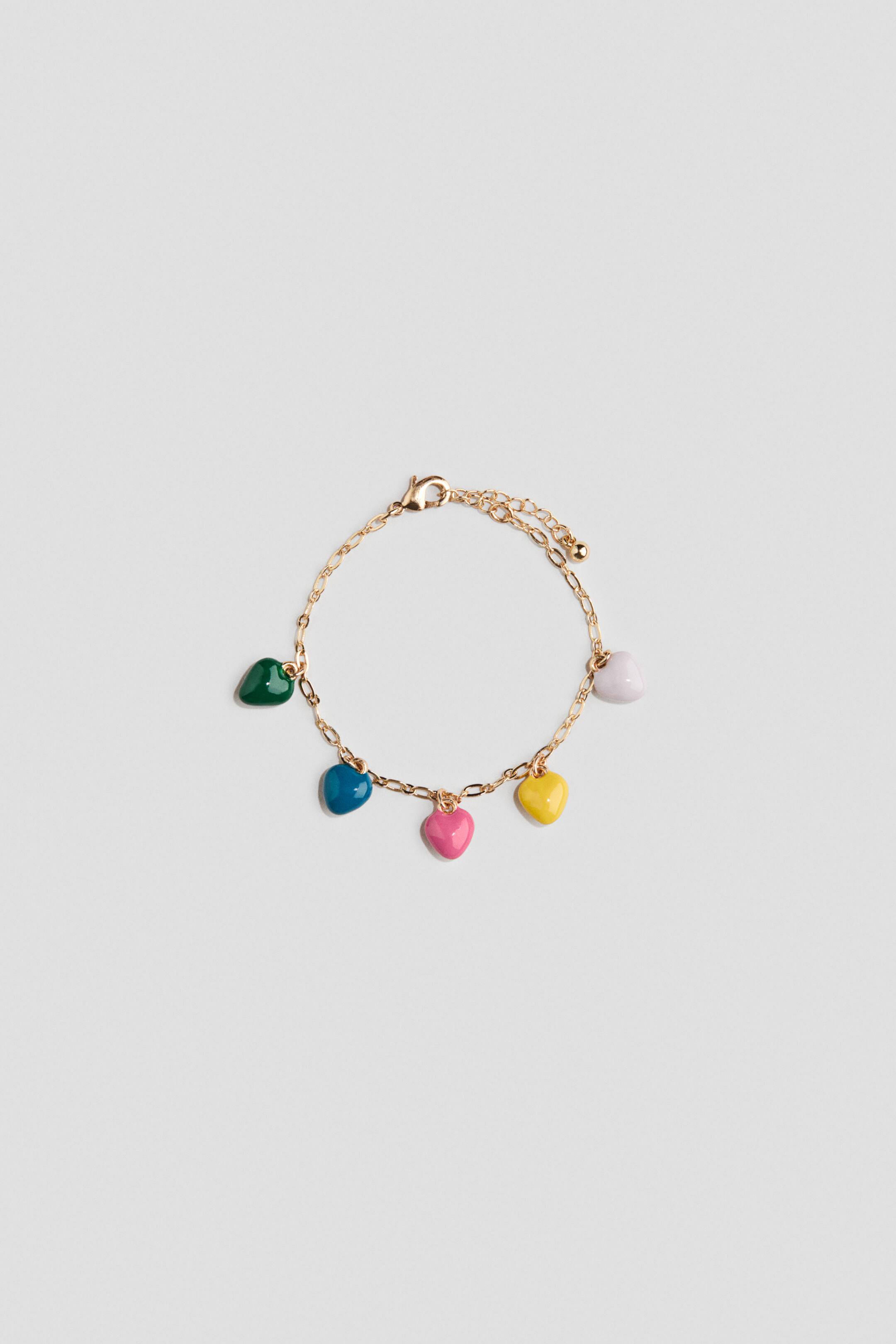 Ver imagem maior: A pulseira exibe uma corrente de tom dourado com cinco pendentes em forma de coração esmaltados, pendendo em cores verde, azul, rosa, amarelo e branco. Um fecho de lagosta e uma corrente extensora ajustável completam o design da pulseira.